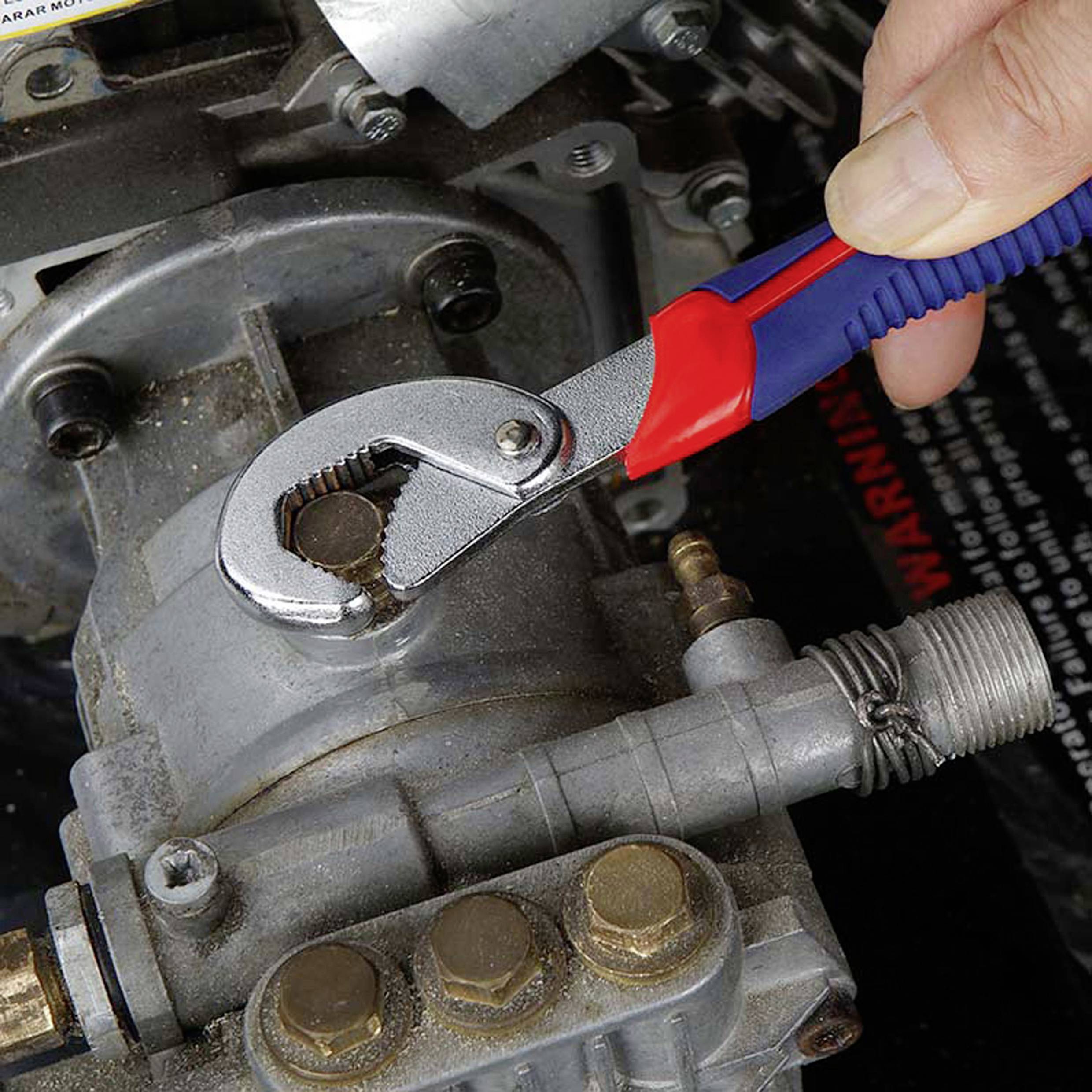 Eine Hand verwendet einen blau-roten verstellbaren Schraubenschlüssel, um eine Schraube an einem Metallteil einer Maschine festzuziehen und zeigt dabei Werkzeuggebrauch und Wartung.