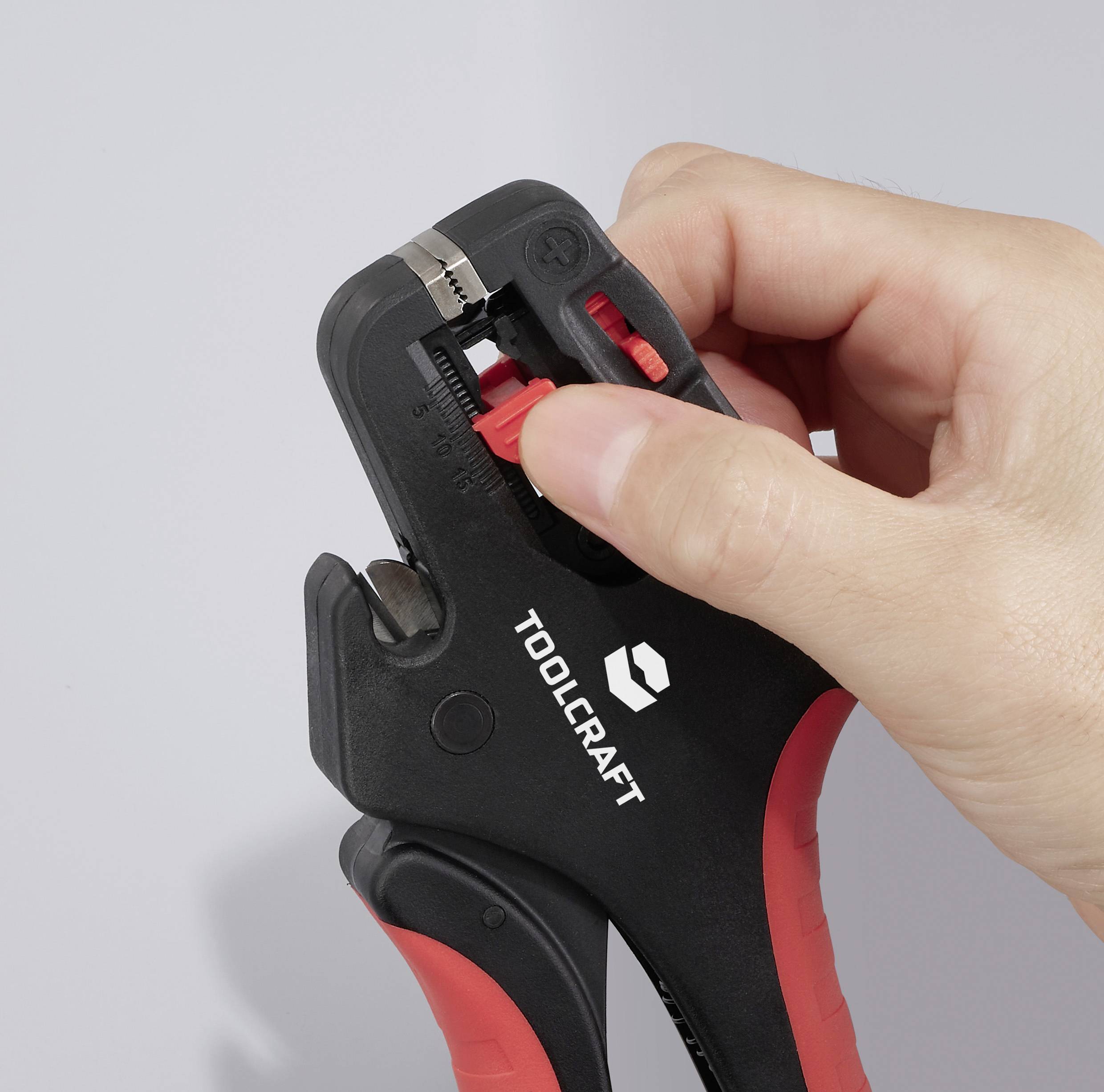 Eine Hand hält einen TOOLCRAFT Verstellschlüssel mit roten Griffen und demonstriert den Verstellmechanismus vor einem neutralen Hintergrund.