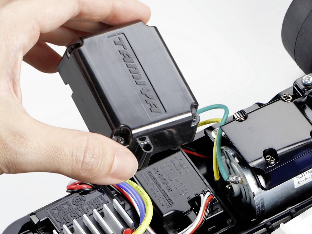 Hand hält ein schwarzes elektronisches Gerät mit Drähten über einer Motorstruktur.