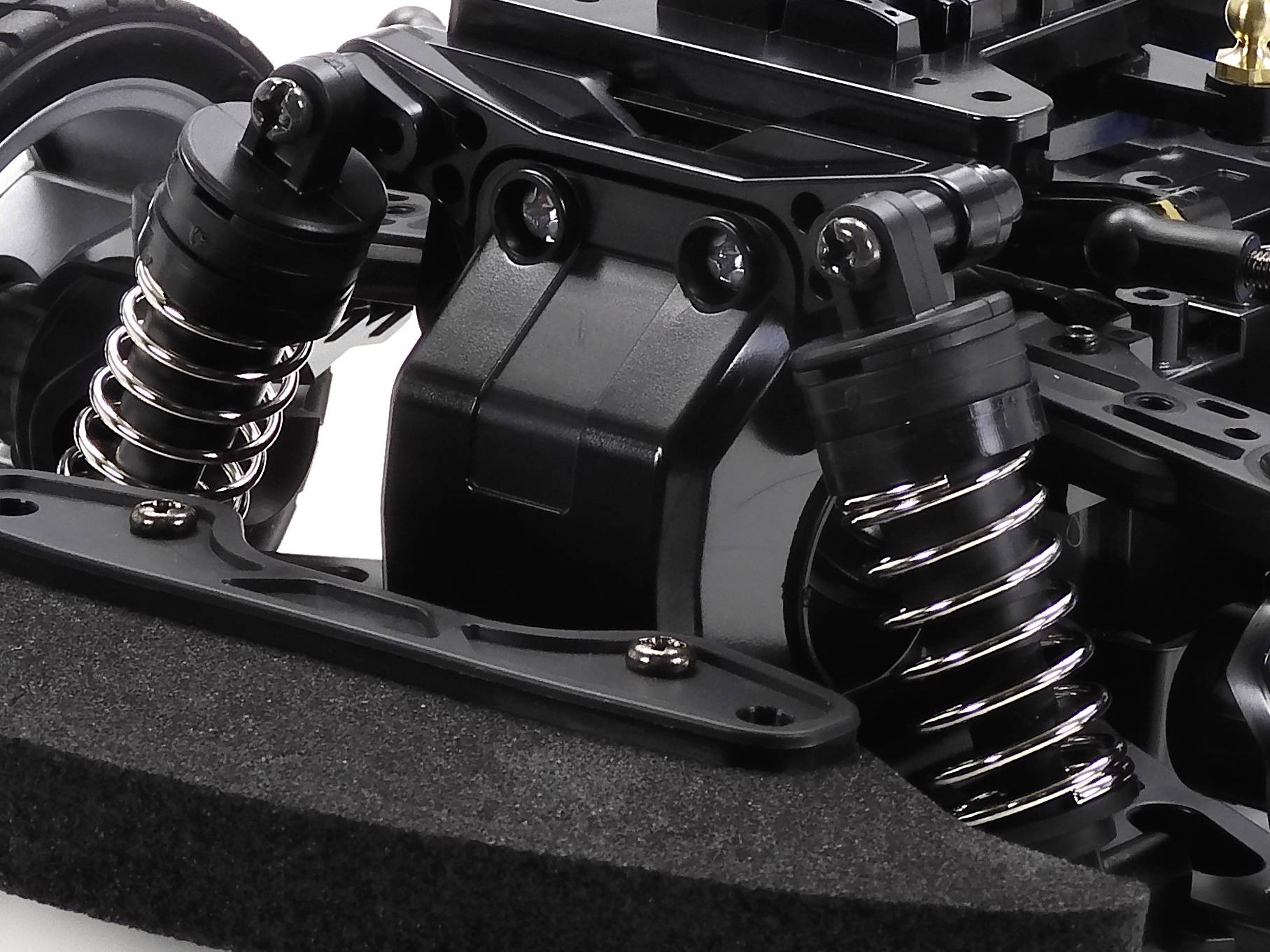 Nahaufnahme eines schwarz gefärbten RC-Auto-Fahrwerks mit Stoßdämpfern und Radaufhängung, fokussiert auf die vorderen Komponenten.