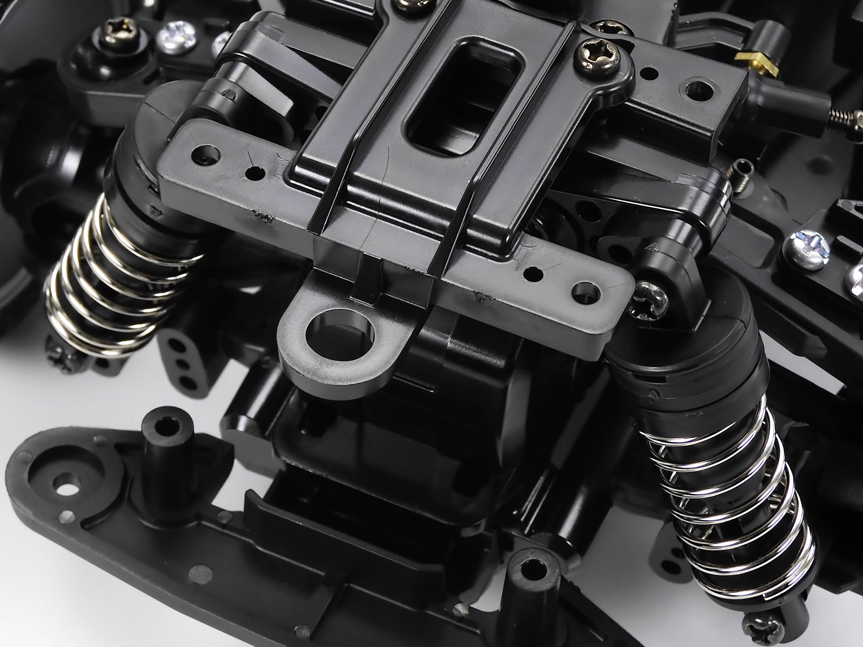 Nahaufnahme eines schwarzen mechanischen Bauteils mit Federn und Schrauben, wahrscheinlich Teil eines Fahrwerks oder Motorsystems.