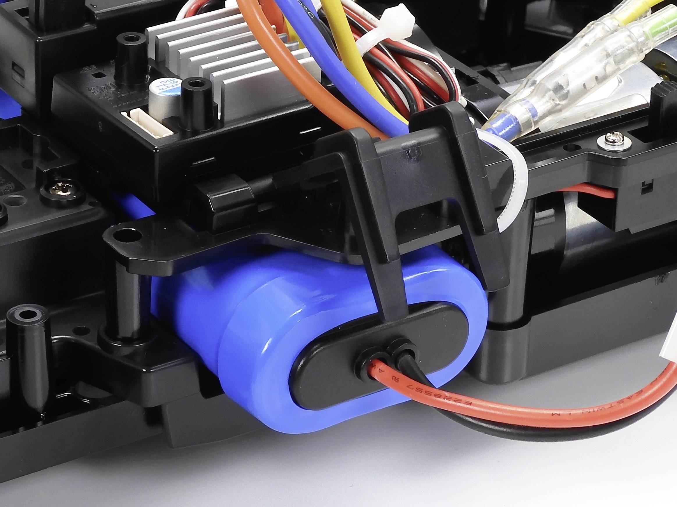 Nahaufnahme eines blauen Akkus mit angeschlossenen roten und schwarzen Kabeln in einem elektronischen Gerät, umgeben von weiteren Bauteilen.