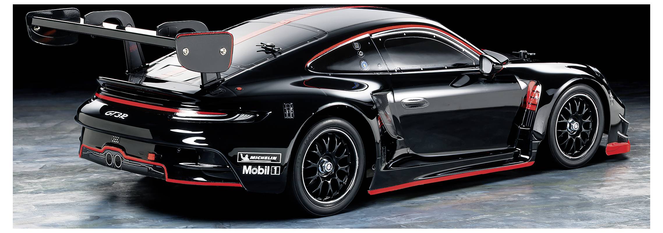 Ein schwarzes Rennfahrzeug mit rotem Akzent, betrachtet von hinten. Es hat einen großen Heckspoiler und Sponsoraufkleber an den Seiten.