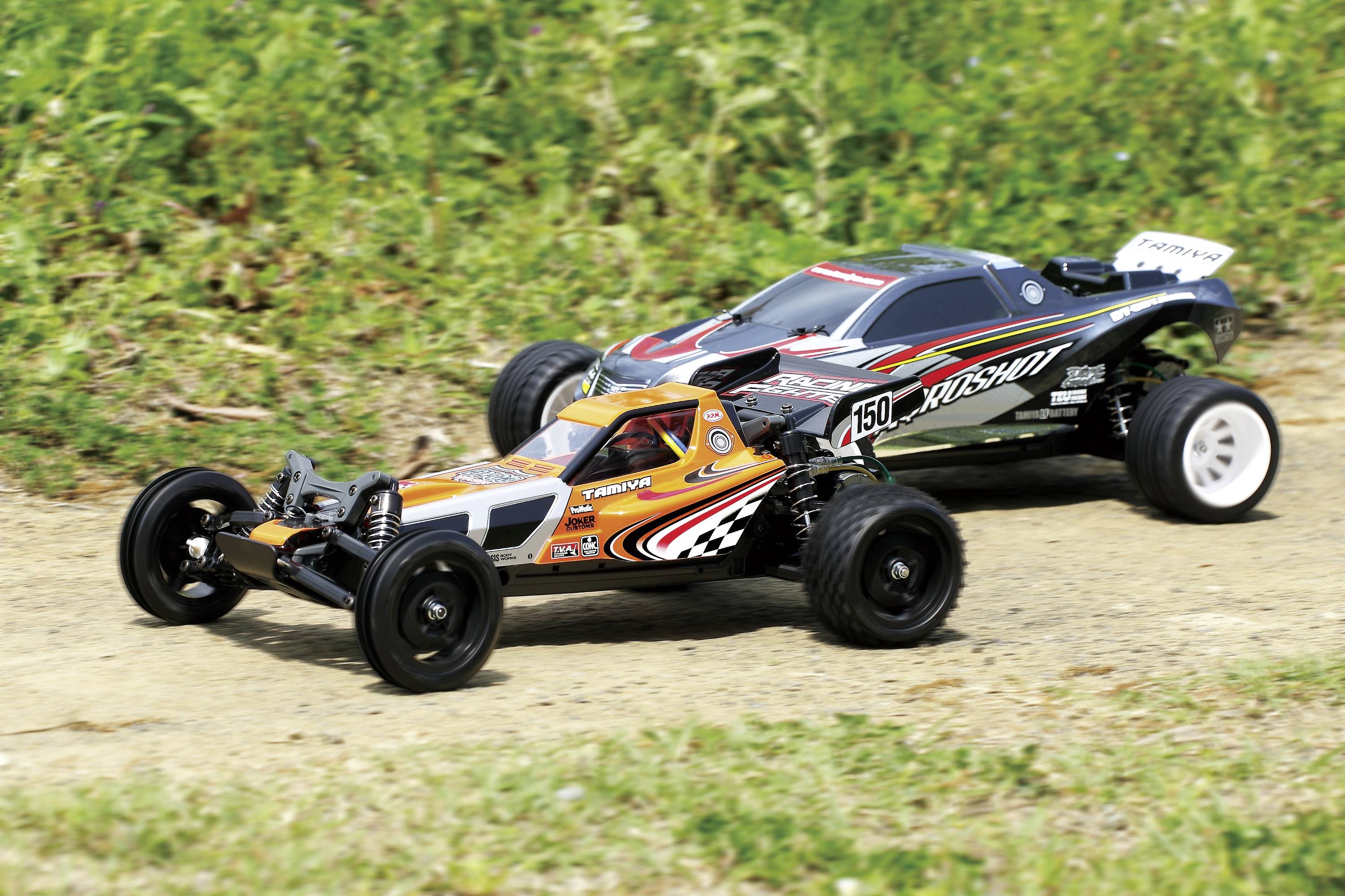 Zwei ferngesteuerte Autos auf einer Rennstrecke im Freien, beide mit auffälligen Designs. Das vordere Auto hat orange und schwarze Muster.