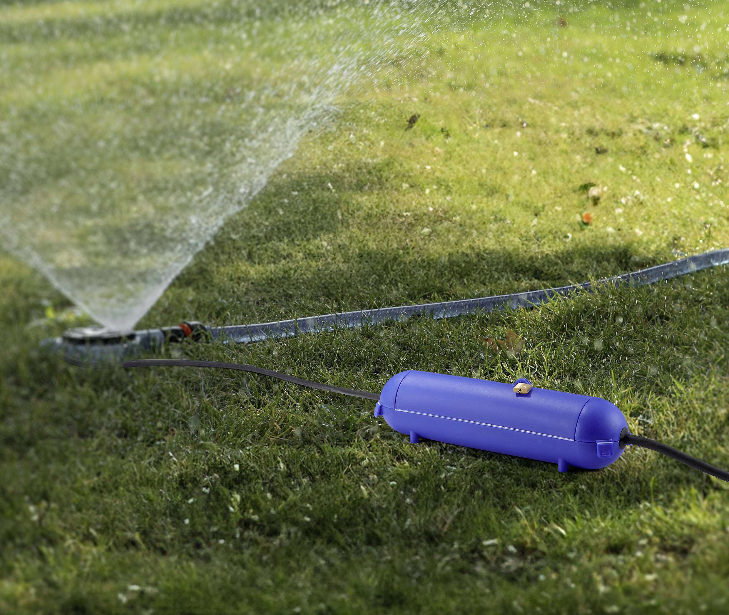 Ein blauer Schlauchanschluss auf Rasen, verbunden mit einem Schlauch, der Wasser in einem breiten Bogen versprüht.
