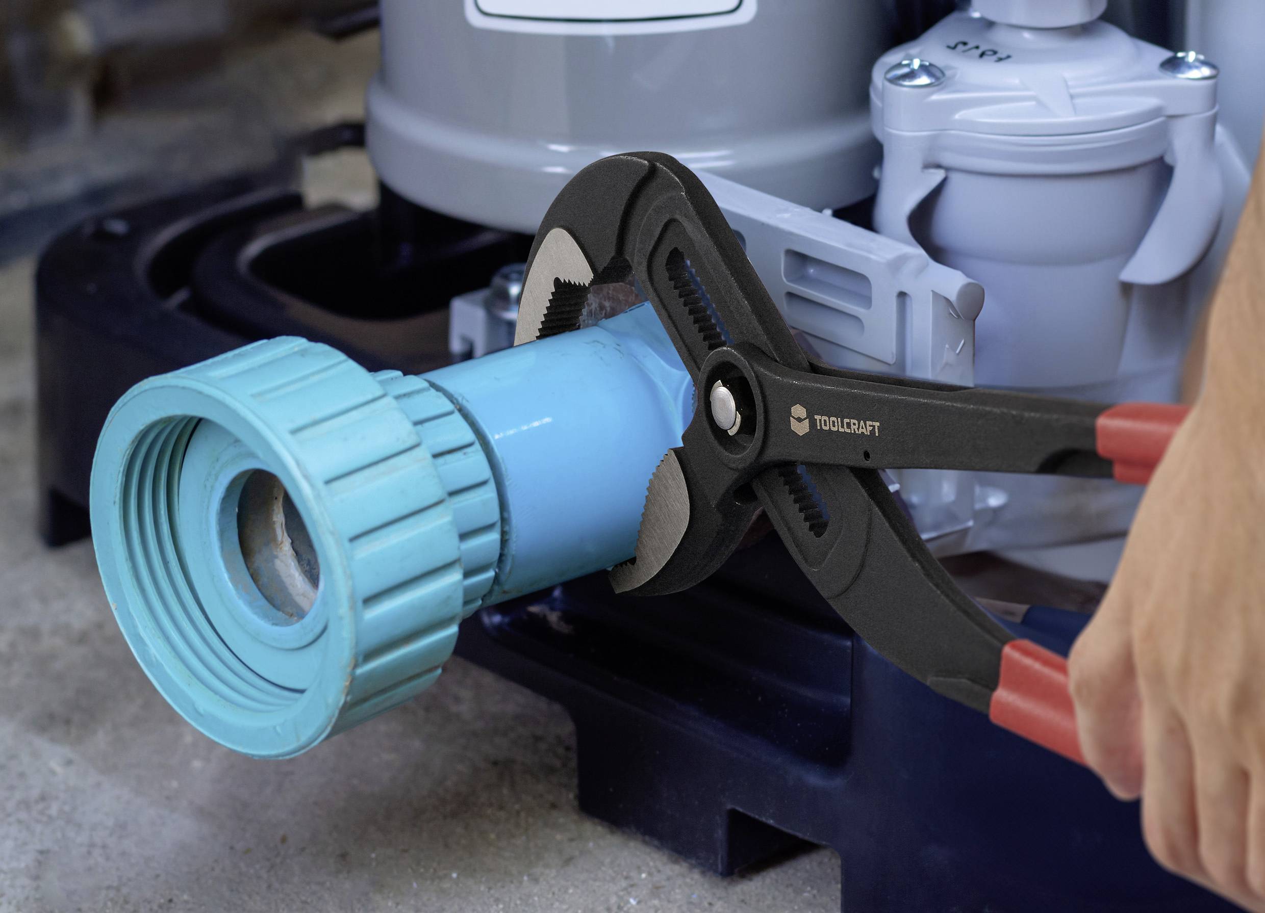 Eine Person verwendet einen großen Schraubenschlüssel, um einen blauen Kunststoff-Rohranschluss an industrieller Ausrüstung festzuziehen, was Wartungs- oder Reparaturarbeiten andeutet.