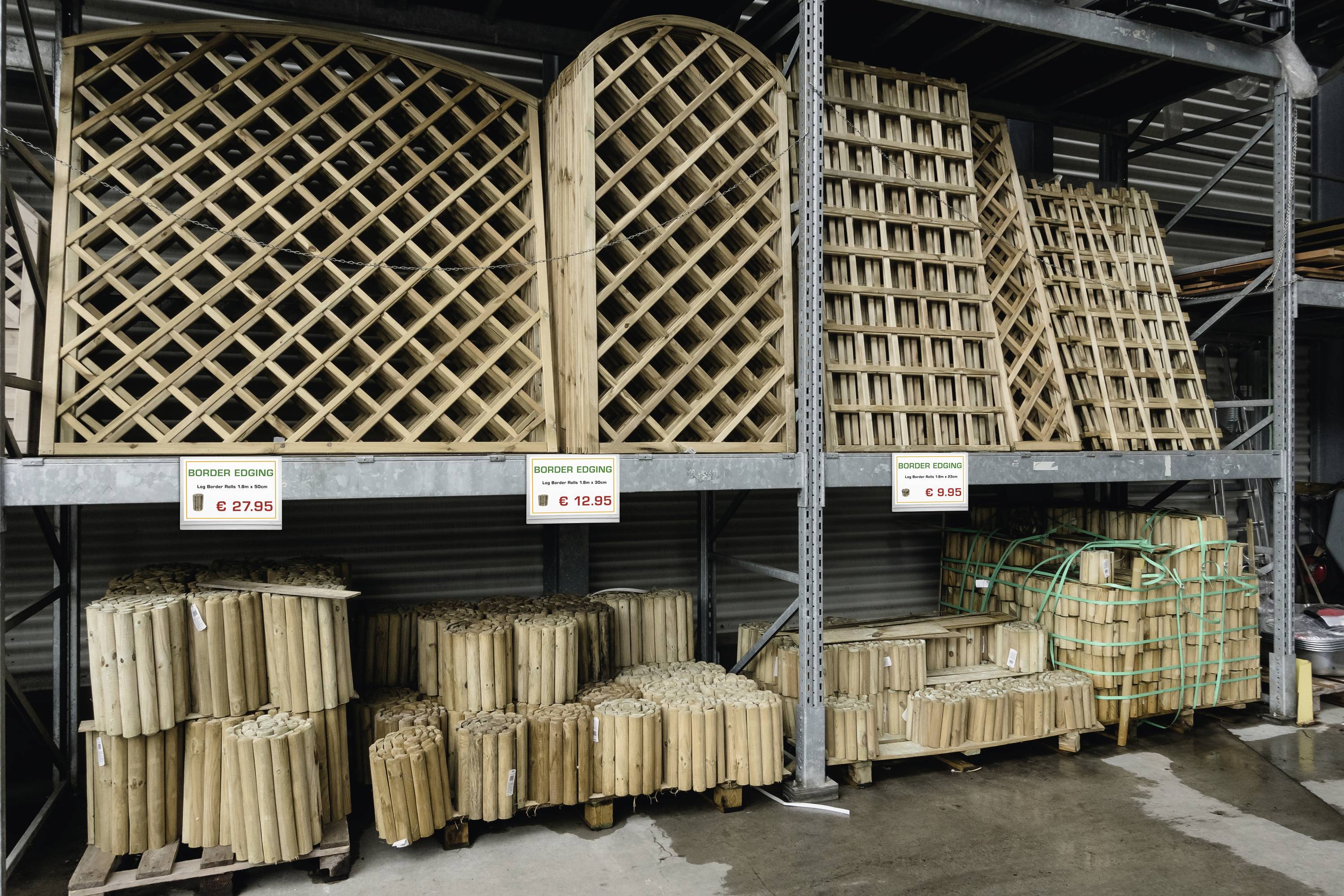 Regale aus Holzgittern in einem Baumarkt mit Preisschildern. Verschiedene Größen und Formen auf zwei Ebenen gestapelt.