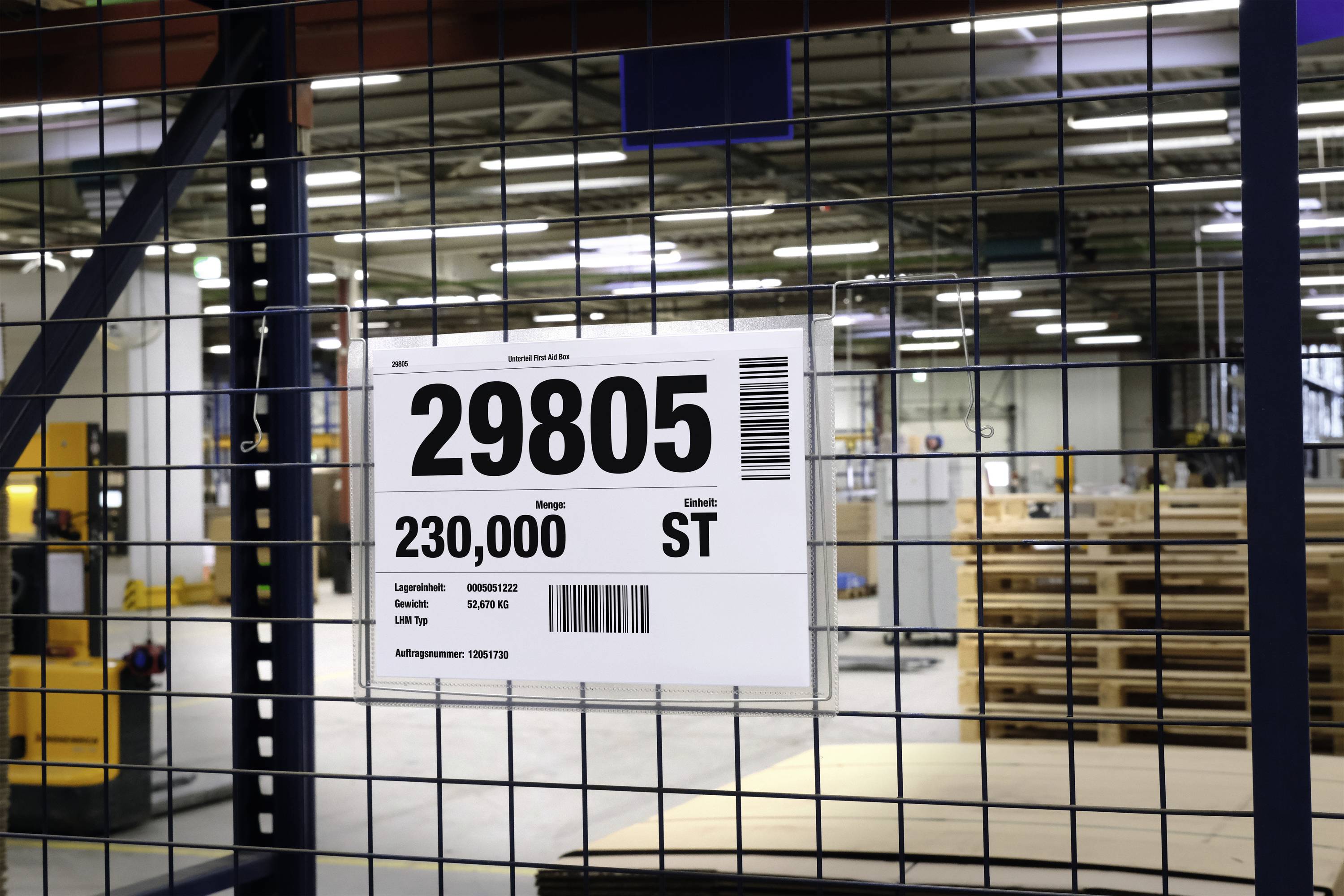 Ein Schild mit der Aufschrift '29805 ST', auf Lagerregal montiert, zeigt die Mengenangabe 230.000 an. Im Hintergrund eine Lagerhalle.