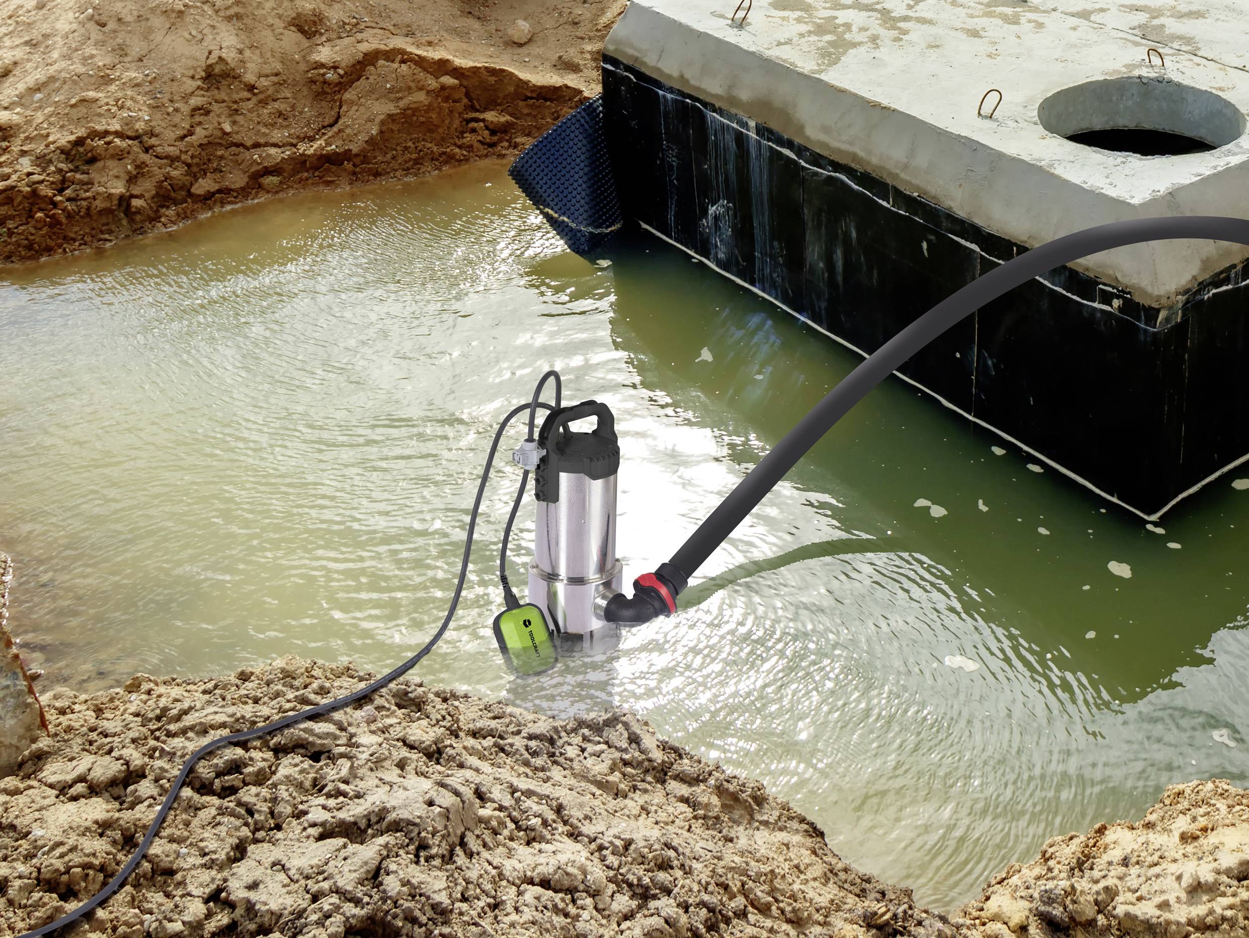 Eine Wasserpumpe entwässert eine Baugrube, indem sie Wasser aus einem betonierten Bereich pumpt. Baustelle erkennbar im Hintergrund.