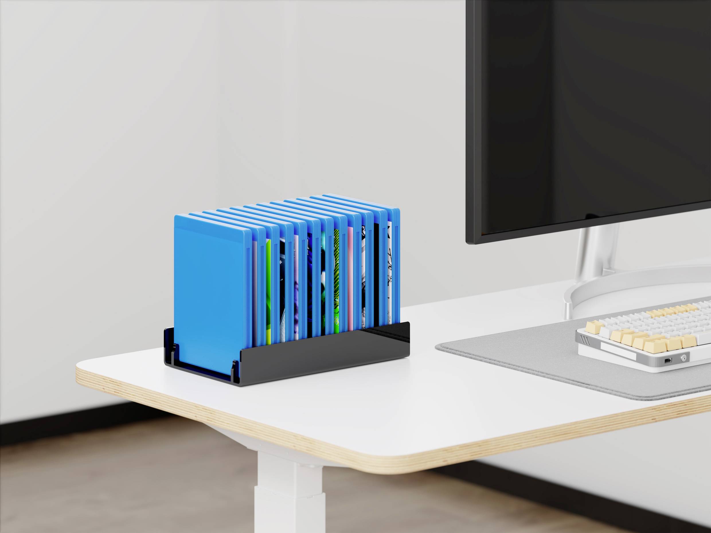 Blaue Aktenordner in einem schwarzen Organizer auf einem weißen Schreibtisch neben einem Computermonitor.