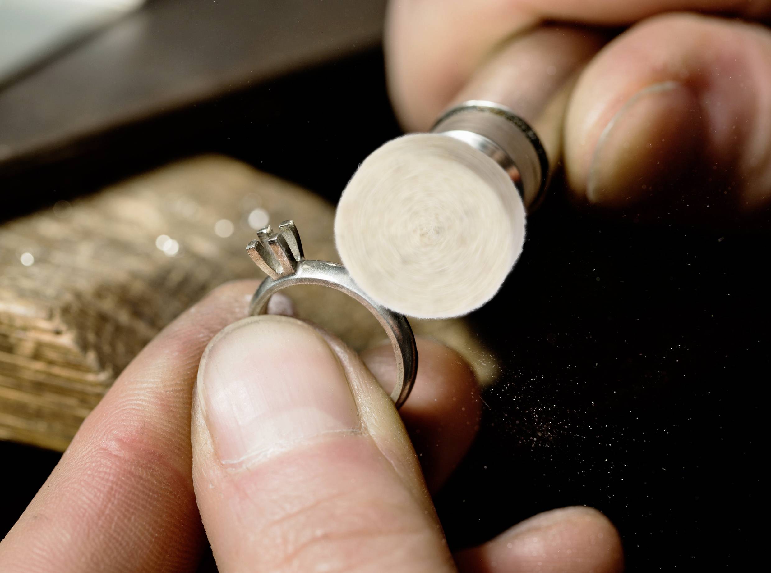 Eine Person, die einen Silberring mit einem Polierwerkzeug poliert und sich auf die Ringfassung konzentriert, was Schmuckhandwerk oder -reparatur andeutet.