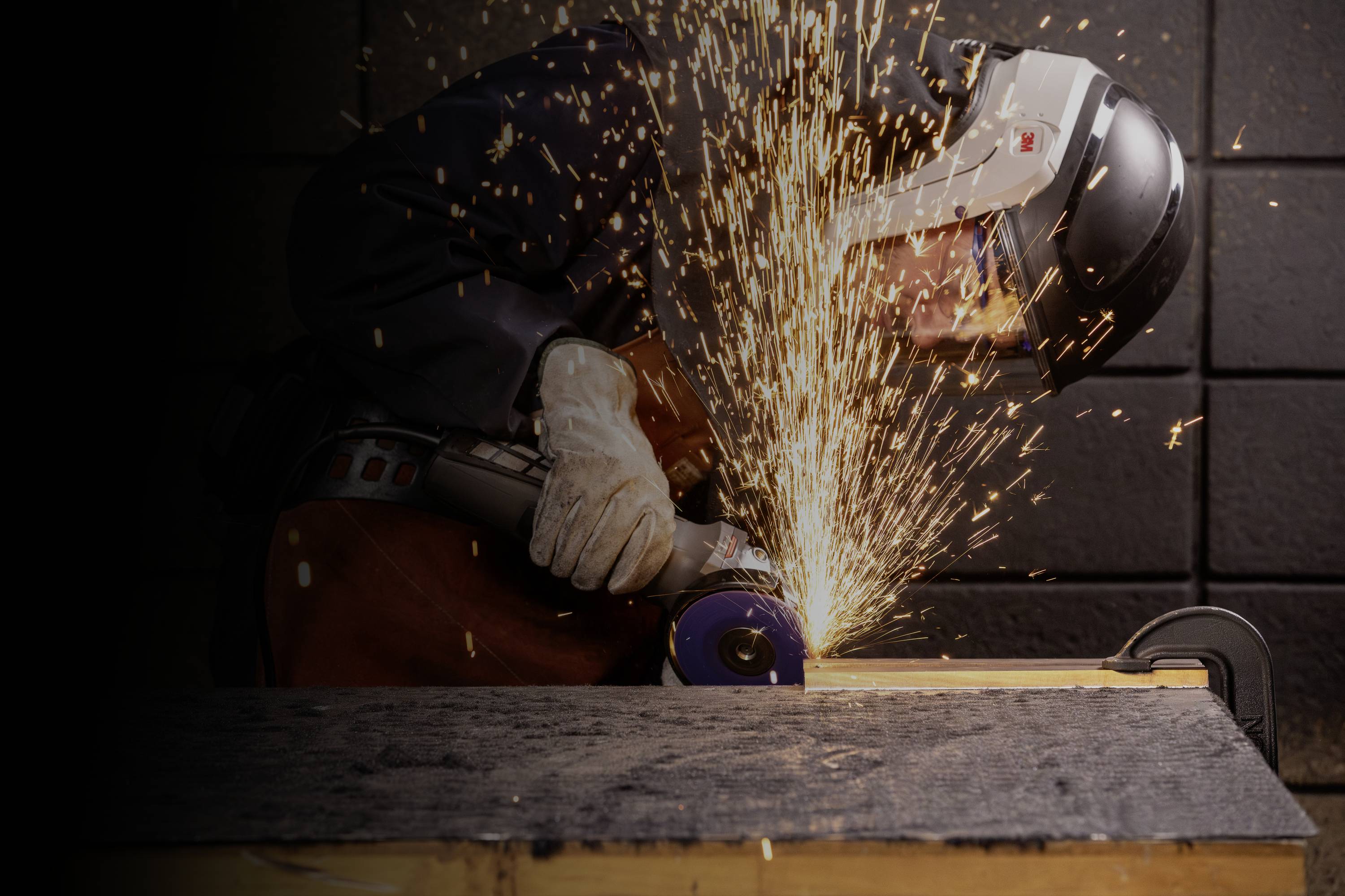 Eine Person trägt Schutzkleidung und benutzt einen Winkelschleifer, während Funken sprühen.