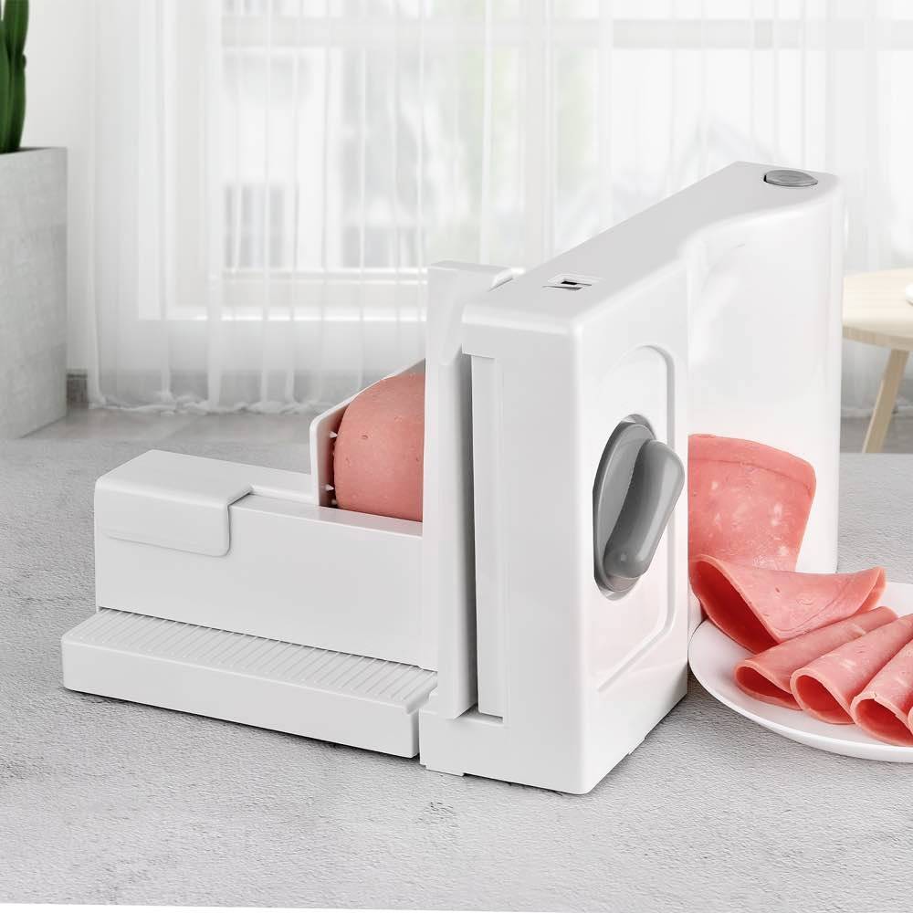 Elektrischer Allesschneider mit rosa Scheiben Wurst auf einem Tisch, vor einem hellen Fenster.