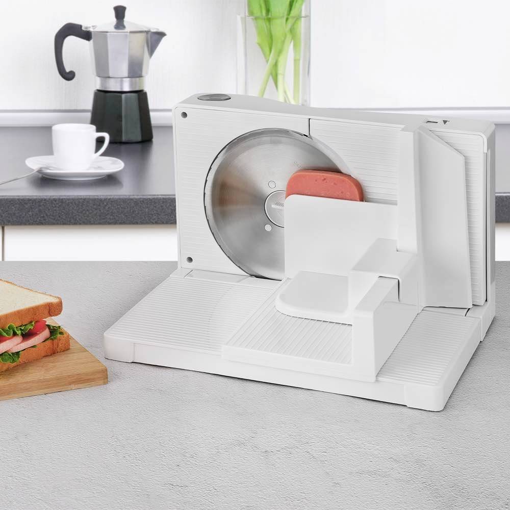 Elektrischer Allesschneider auf einer Küchenarbeitsplatte, bereit zum Schneiden von Brot. Im Hintergrund Kaffeemaschine und Tasse.