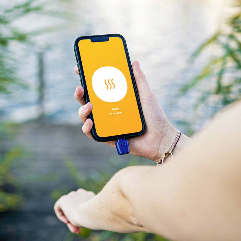 Eine Person hält ein Smartphone. Auf dem Bildschirm steht 'Heating' sowie eine Anzeige '55%' vor einem unscharfen See im Hintergrund.