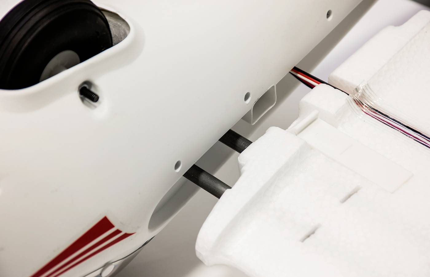 Detailaufnahme einer weißen Modellflugzeugstruktur mit verbundenen Flügeln und sichtbaren elektronischen Verkabelungen.