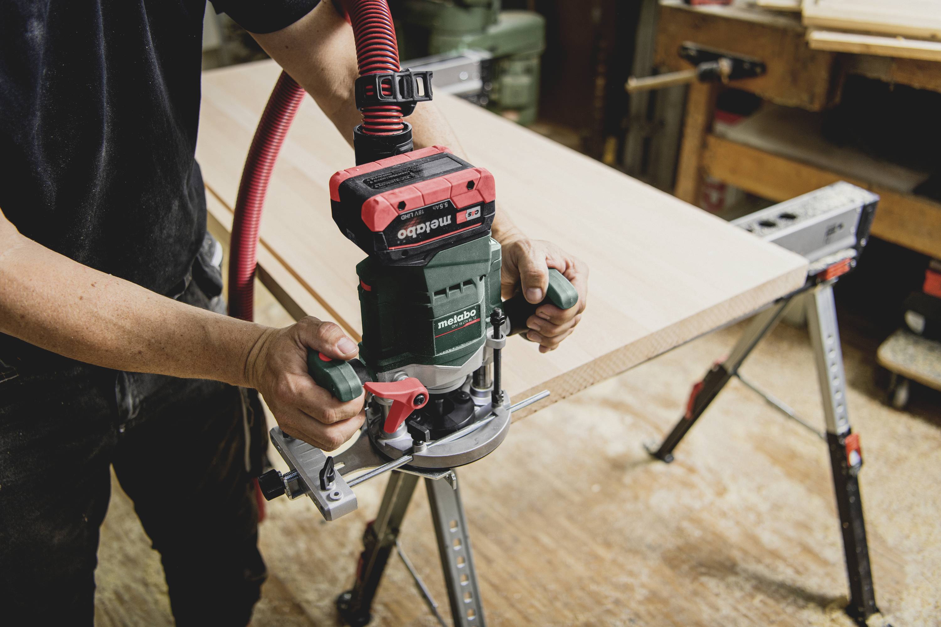Eine Person benutzt eine Oberfräse, um die Kante eines Holzbalkens in einer Werkstatt zu bearbeiten.