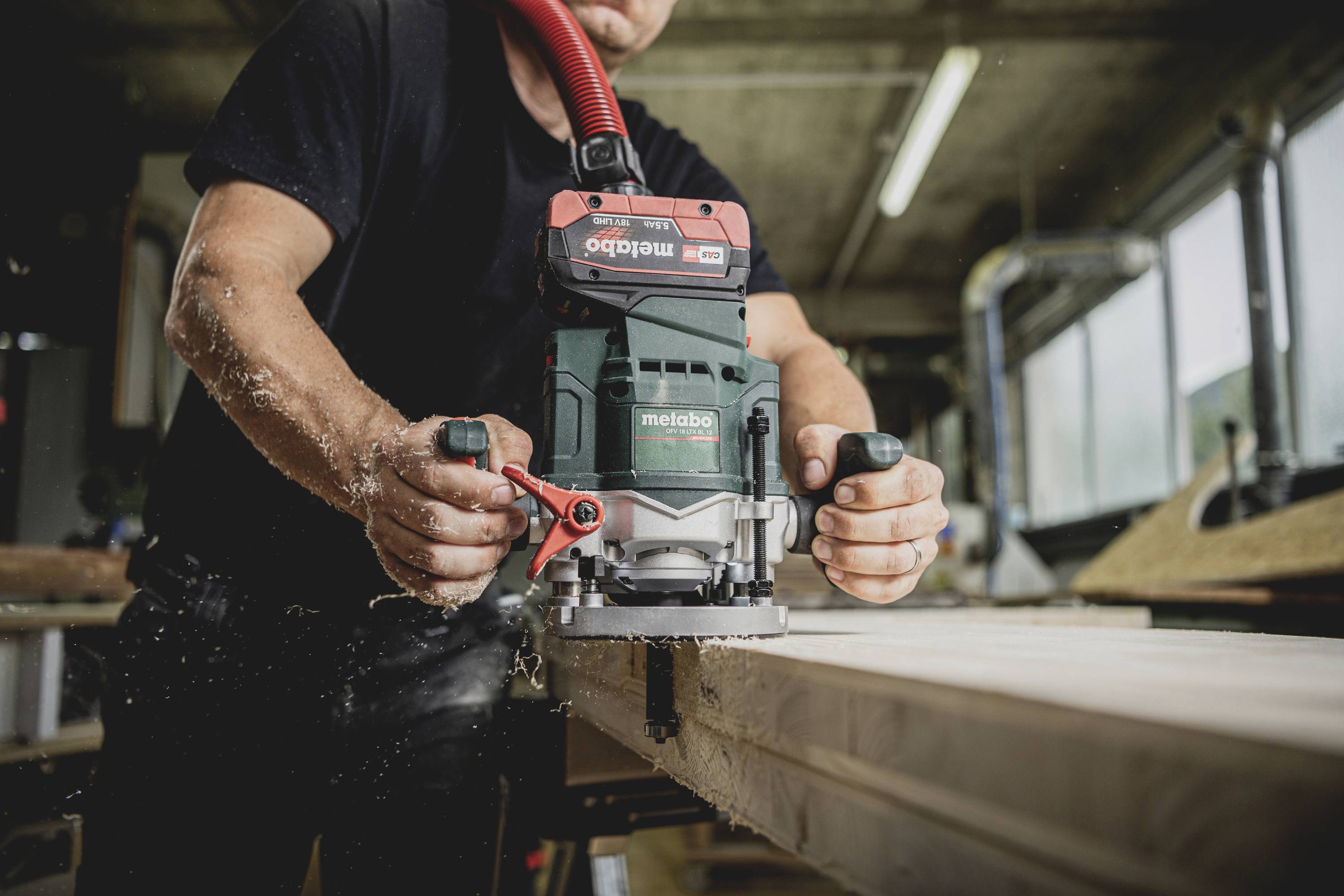 Eine Person arbeitet mit einem grünen elektrischen Holzbearbeitungsgerät auf einem Holzbrett in einer Werkstattumgebung.