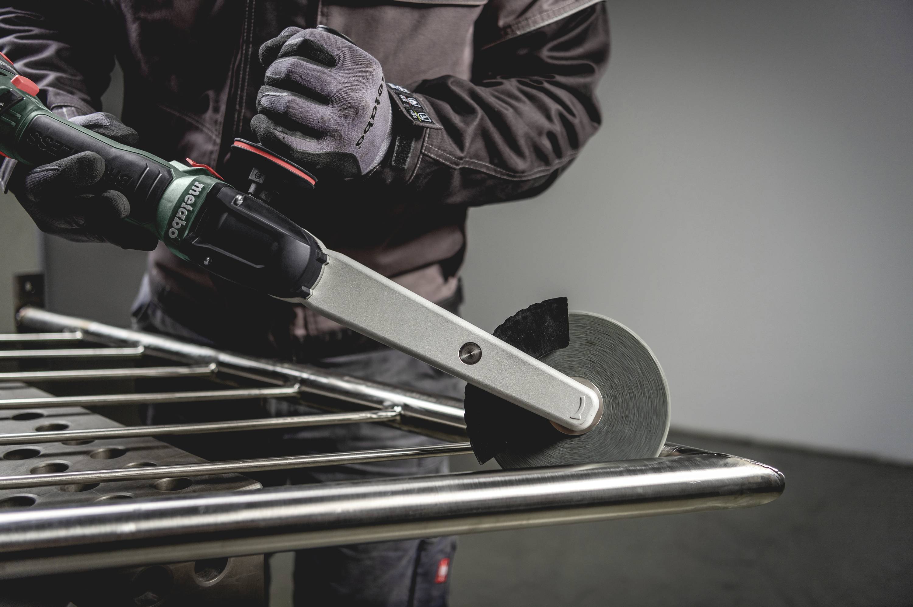 Person arbeitet mit einem Winkelpolierer an einem Metallgeländer, trägt Schutzkleidung und Handschuhe.