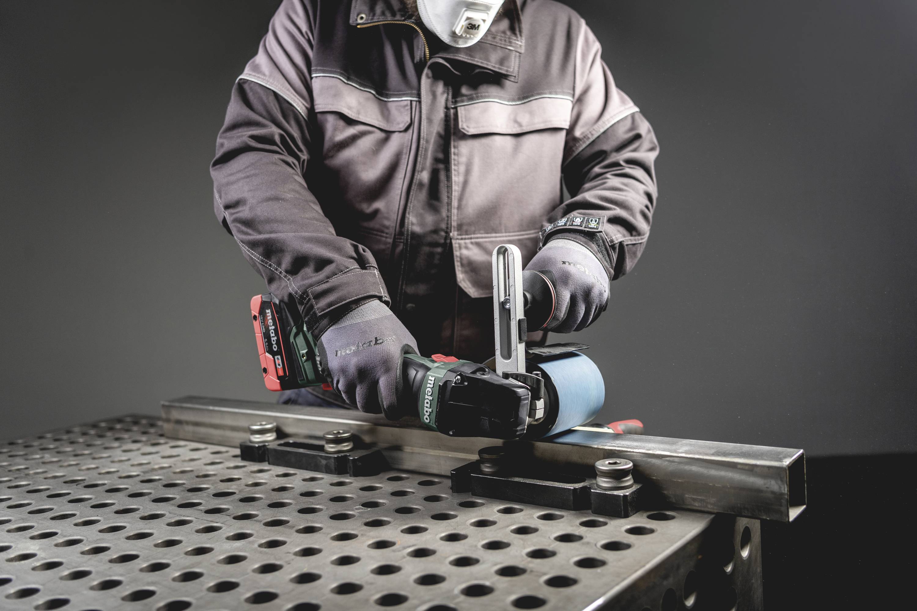 Eine Person führt eine Metallbearbeitung mit einer Elektrowerkzeugmaschine auf einem durchlöcherten Arbeitstisch durch.