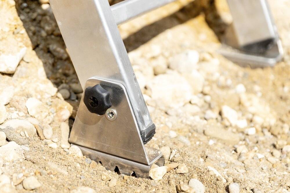 Nahaufnahme eines stabilen Metalltreppenfußes, der sicher auf einem kiesigen Untergrund steht. Geeignet für den Einsatz in unebenem Gelände.