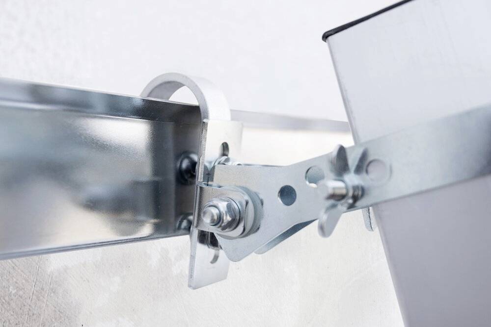 Metallhalterung, die eine rechteckige Rinne an einem Rohr befestigt. Silberfarben mit Schrauben zur Stabilisierung.