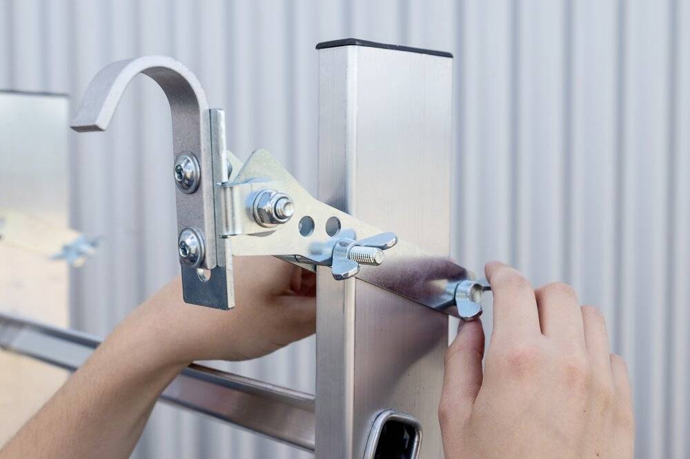 Eine Person montiert eine Metallhalterung an einem quadratischen Metallpfosten mit Schraubenschlüssel.