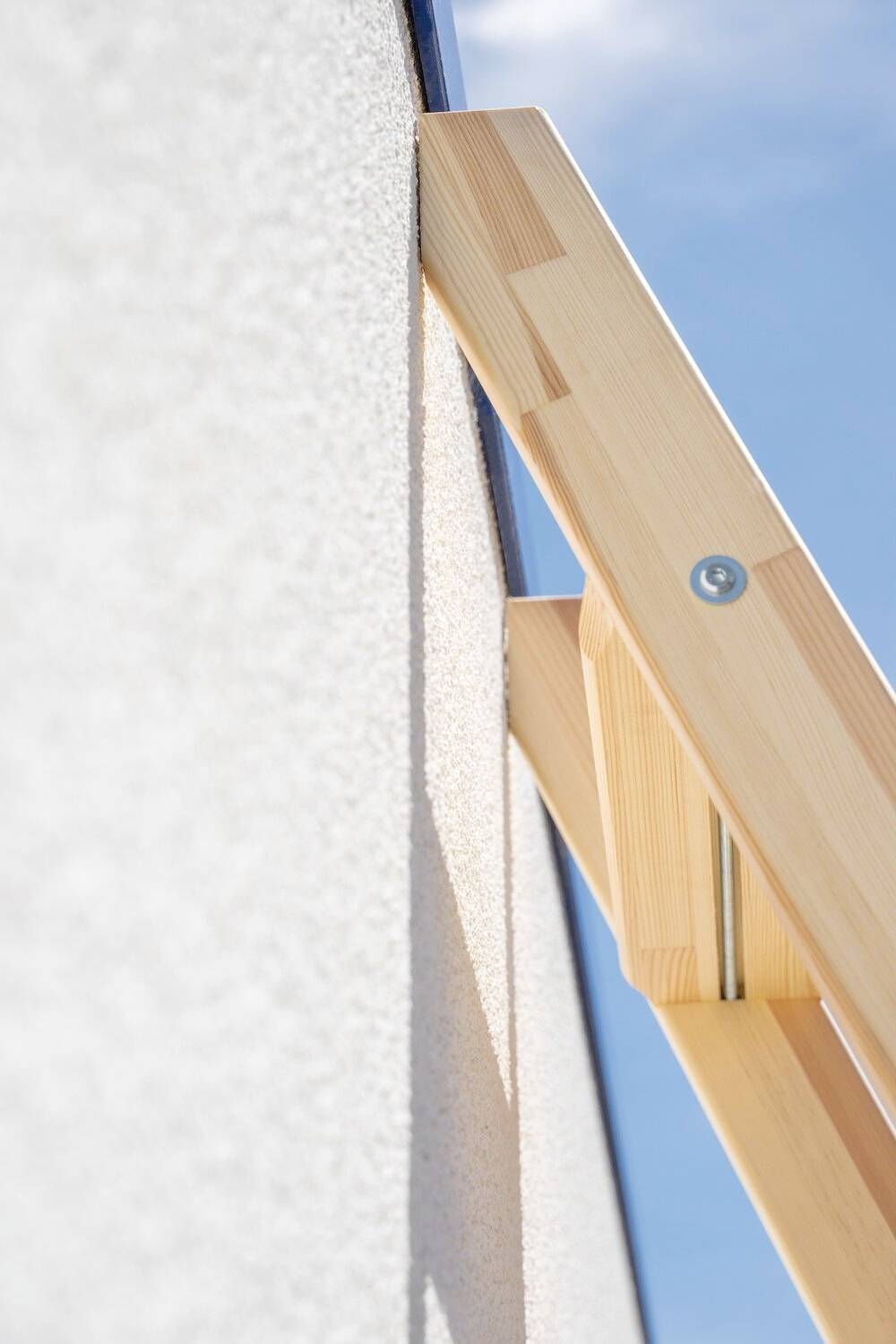 Ein Holzständer lehnt gegen eine Wand. Ein Schraubenkopf ist sichtbar. Der Winkel deutet auf eine Fensterreinigung oder -installation hin.