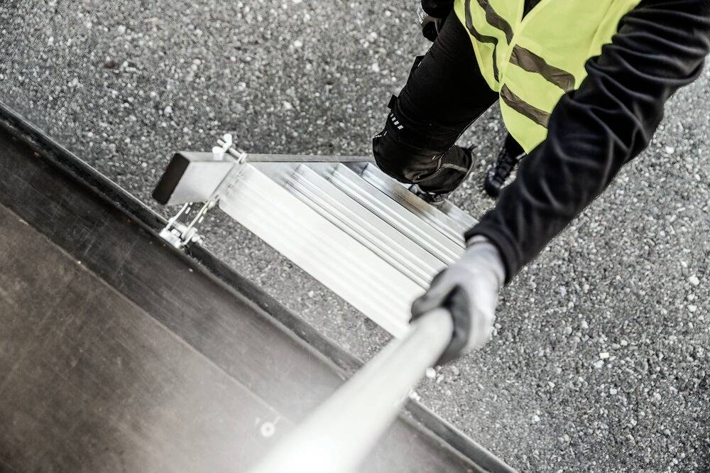 Eine Person in Arbeitskleidung steigt eine Leiter hinauf, die an einem LKW angelehnt ist.