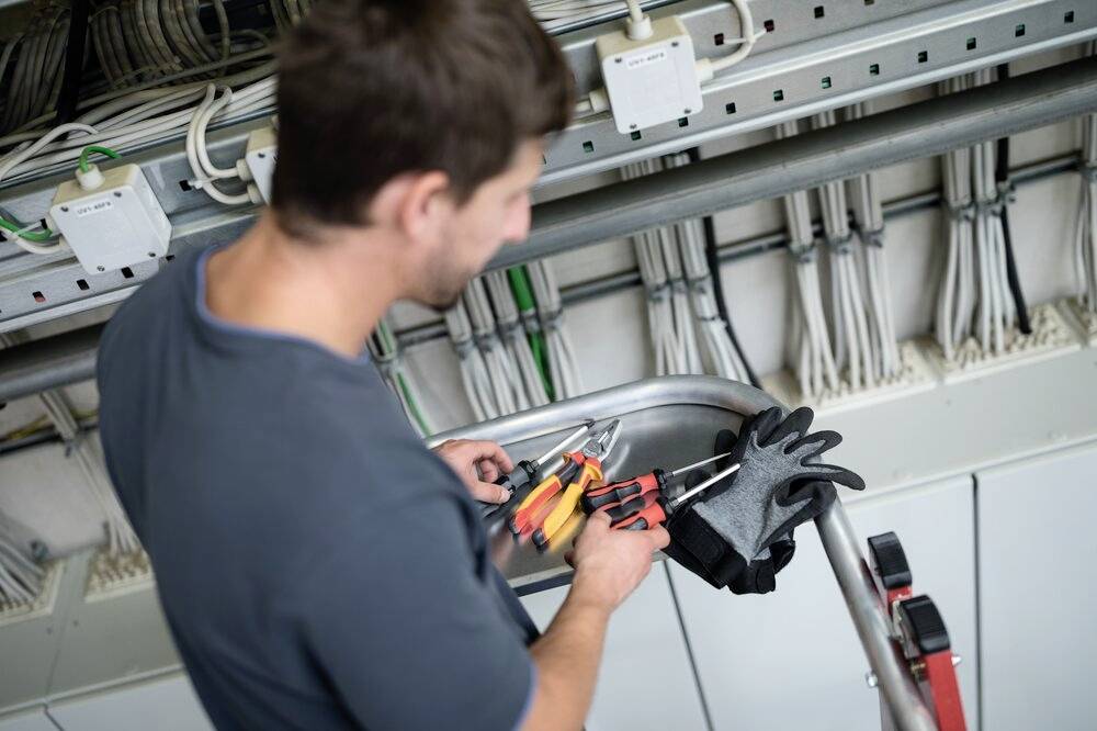 Ein Techniker mit Werkzeugen und Handschuhen repariert Kabel in einer elektrischen Schalttafel.