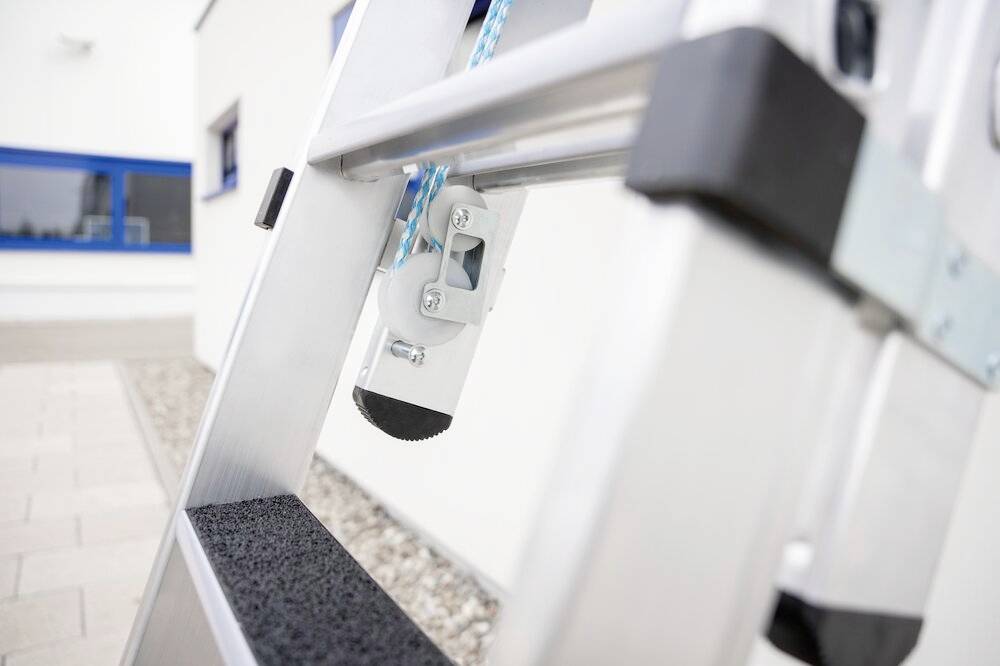 Aluminiumleiter mit rutschfesten Stufen steht an der Fassade eines Gebäudes, seitliche Nahaufnahme der Sicherheitsmechanismen.