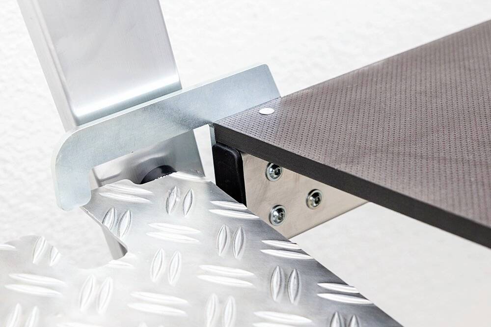 Nahaufnahme einer industriellen Maschine mit Metallplattform und schwarzer Gummimatte, verbunden durch silbern glänzende Schrauben.