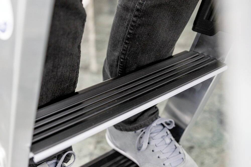 Eine Person steigt auf eine Metallleiter, sichtbar sind Schuhe und die Sprossen der Leiter.