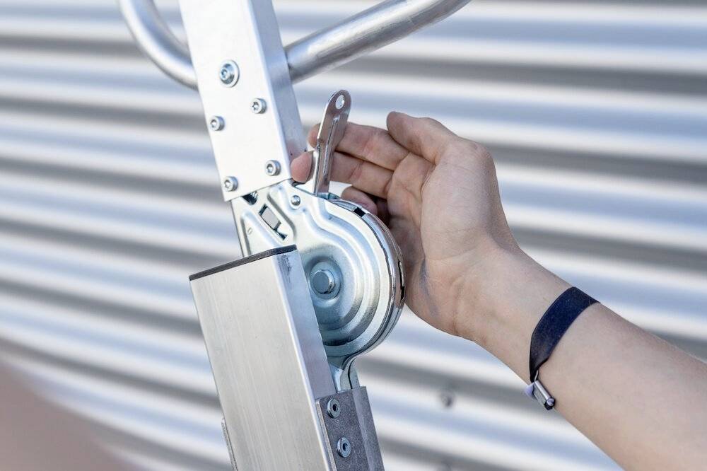 Eine Hand dreht an einer mechanischen Kurbel eines Metallgeräts vor einem gerippten Hintergrund.