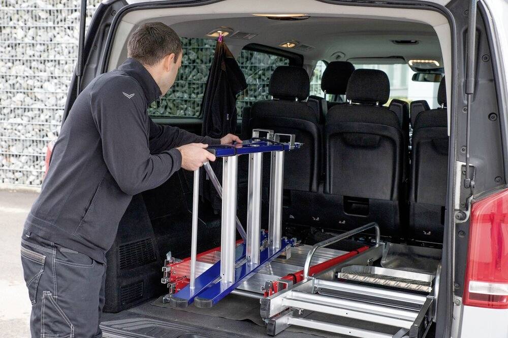 Eine Person lädt eine blaue Rampe in einen Van. Die Rücksitze sind umgeklappt, um Platz zu schaffen.