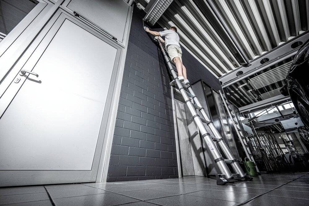 Eine Person steht auf einer hohen Aluminiumleiter in einer modernen Garage und führt Arbeiten an der Decke durch.