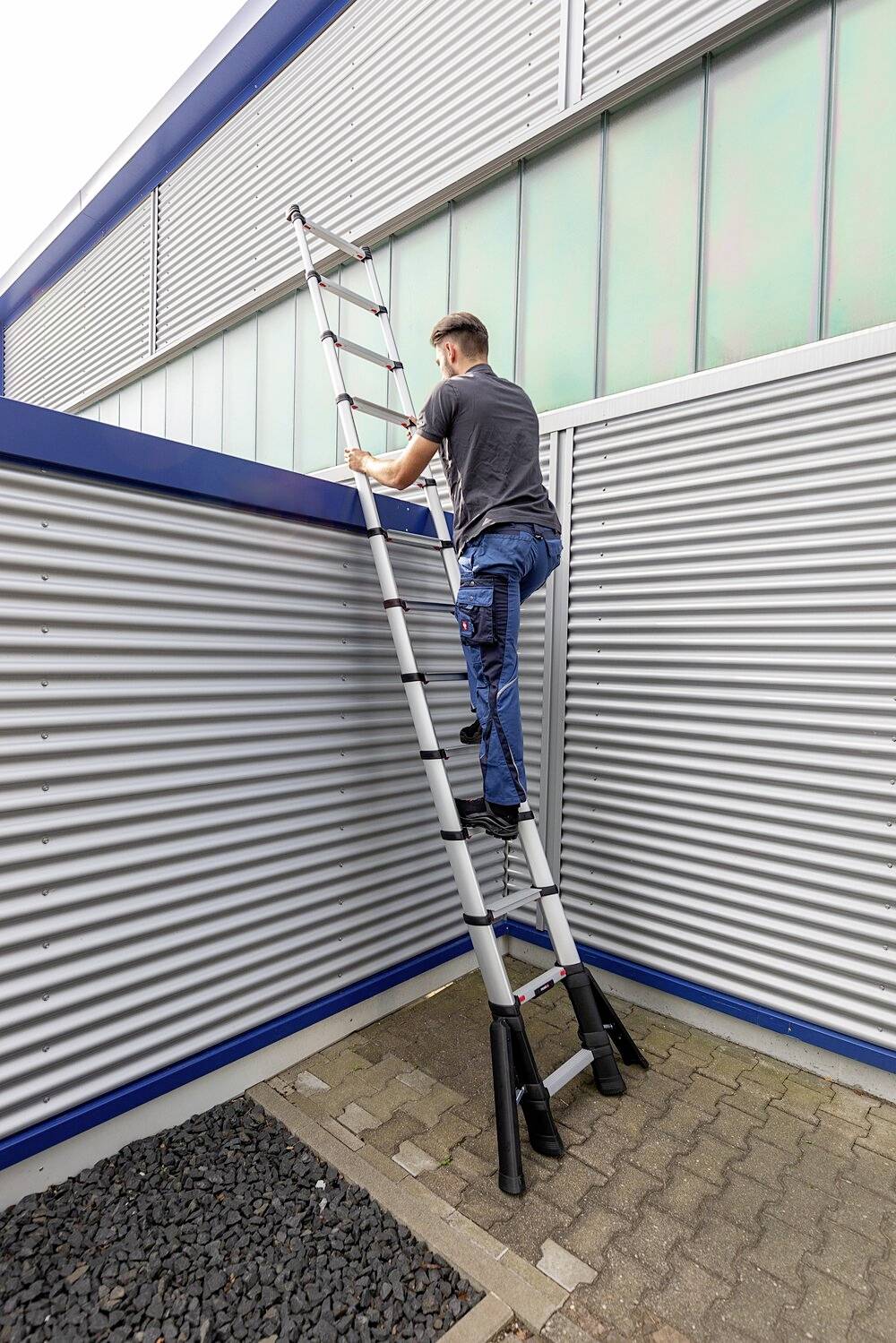 Mann steigt auf Ausziehleiter an metallischer Wand eines Gebäudes.