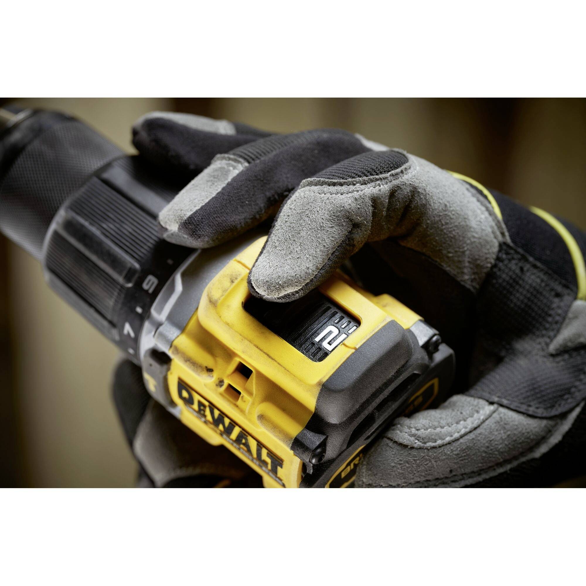 Eine Person trägt schwarze und graue Handschuhe und hält eine elektrische Bohrmaschine mit einem gelben 'DeWalt'-Logo fest.