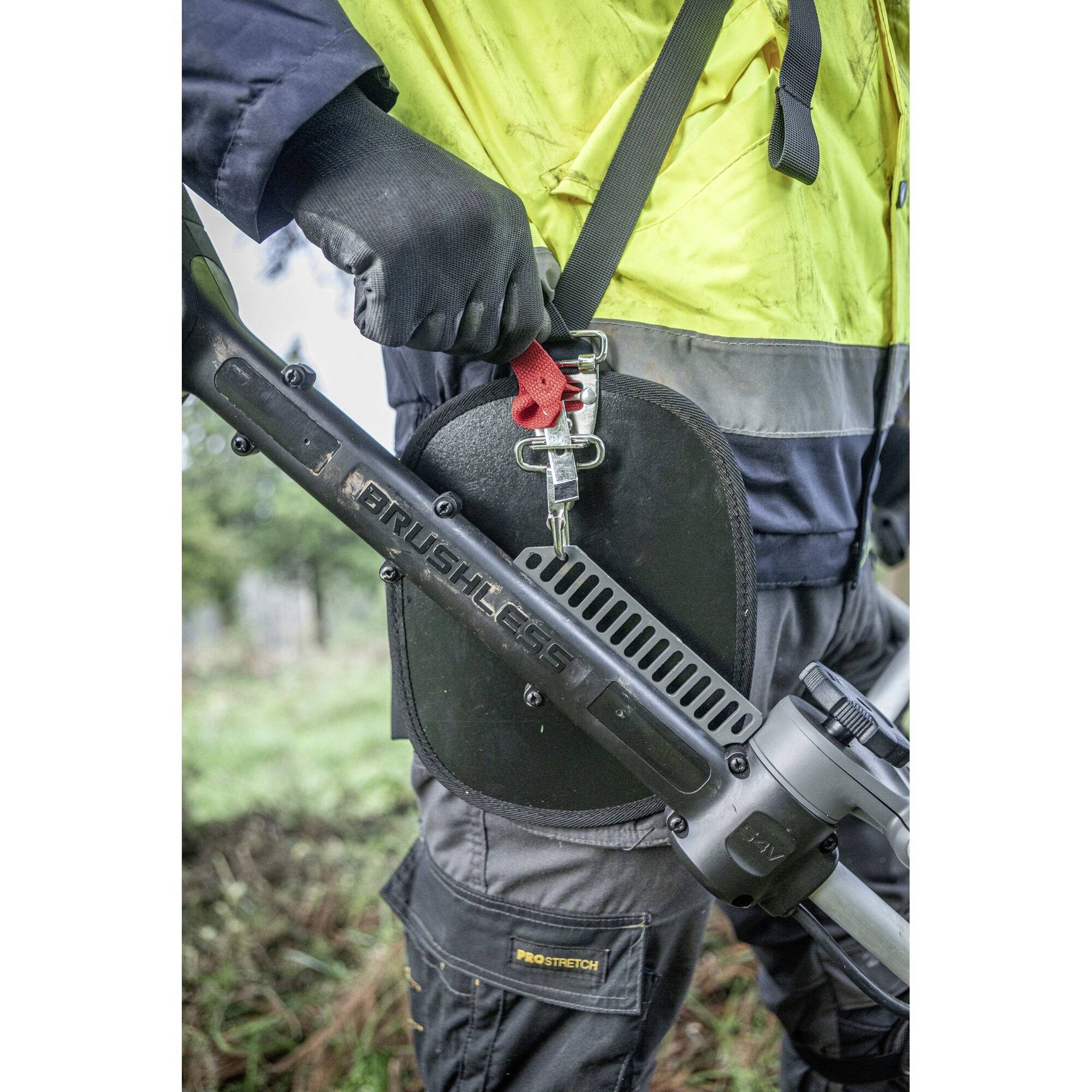 Eine Person in Arbeitskleidung trägt ein elektro-betriebenes Werkzeug im Freien. Das Gerät hat die Aufschrift 'BRUSHLESS'.