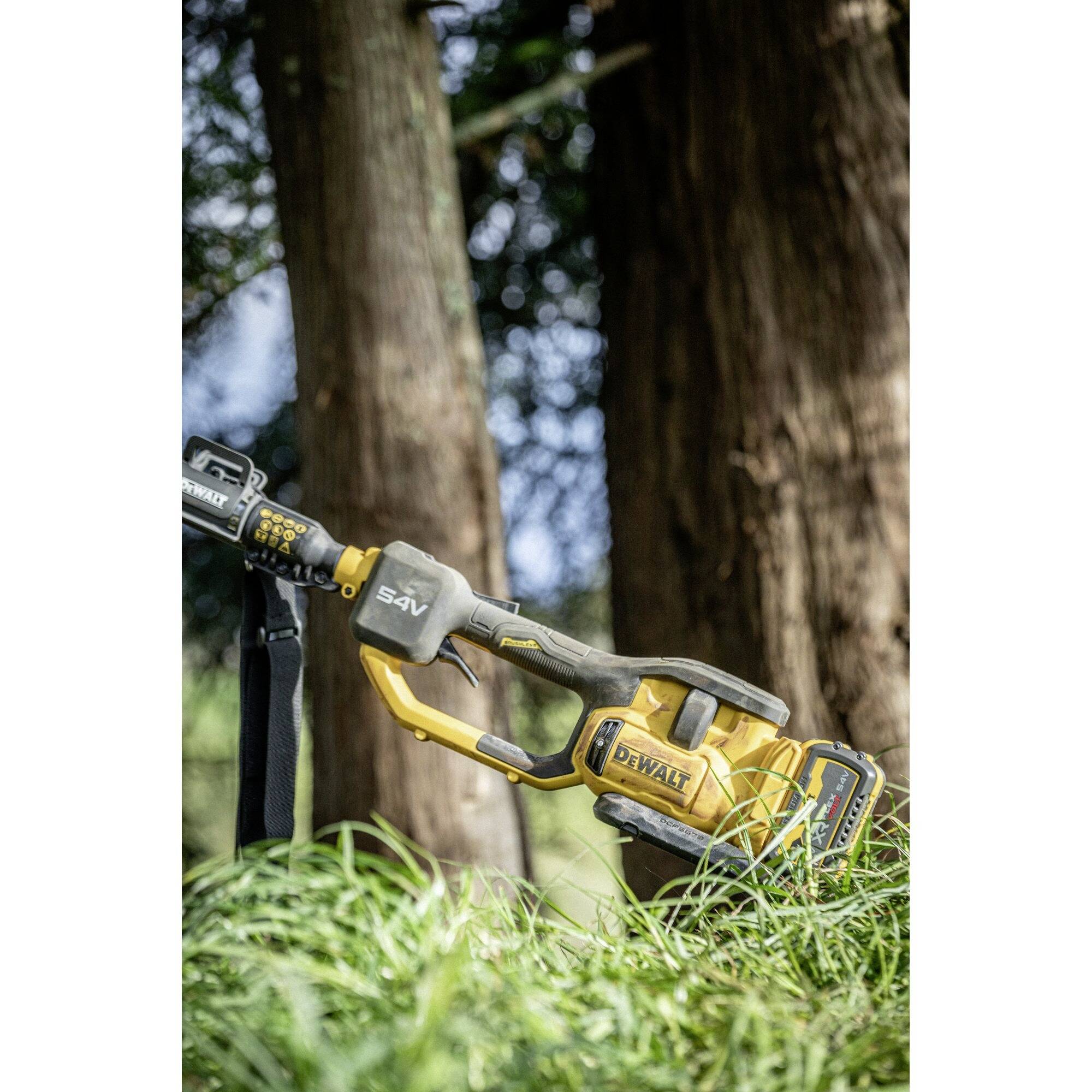 Nahaufnahme einer gelben Kettensäge in hohem Gras, mit Bäumen im Hintergrund. Die Kettensäge ist auf den Einsatz im Wald vorbereitet.