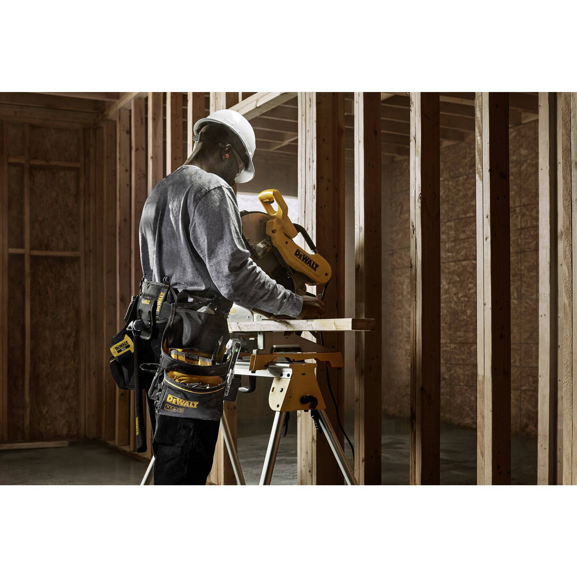 Arbeiter mit Helm bedient elektrische Säge in einem Rohbau, um Holz zu schneiden. Hintergrund zeigt unvollständige Innenwände aus Holz.
