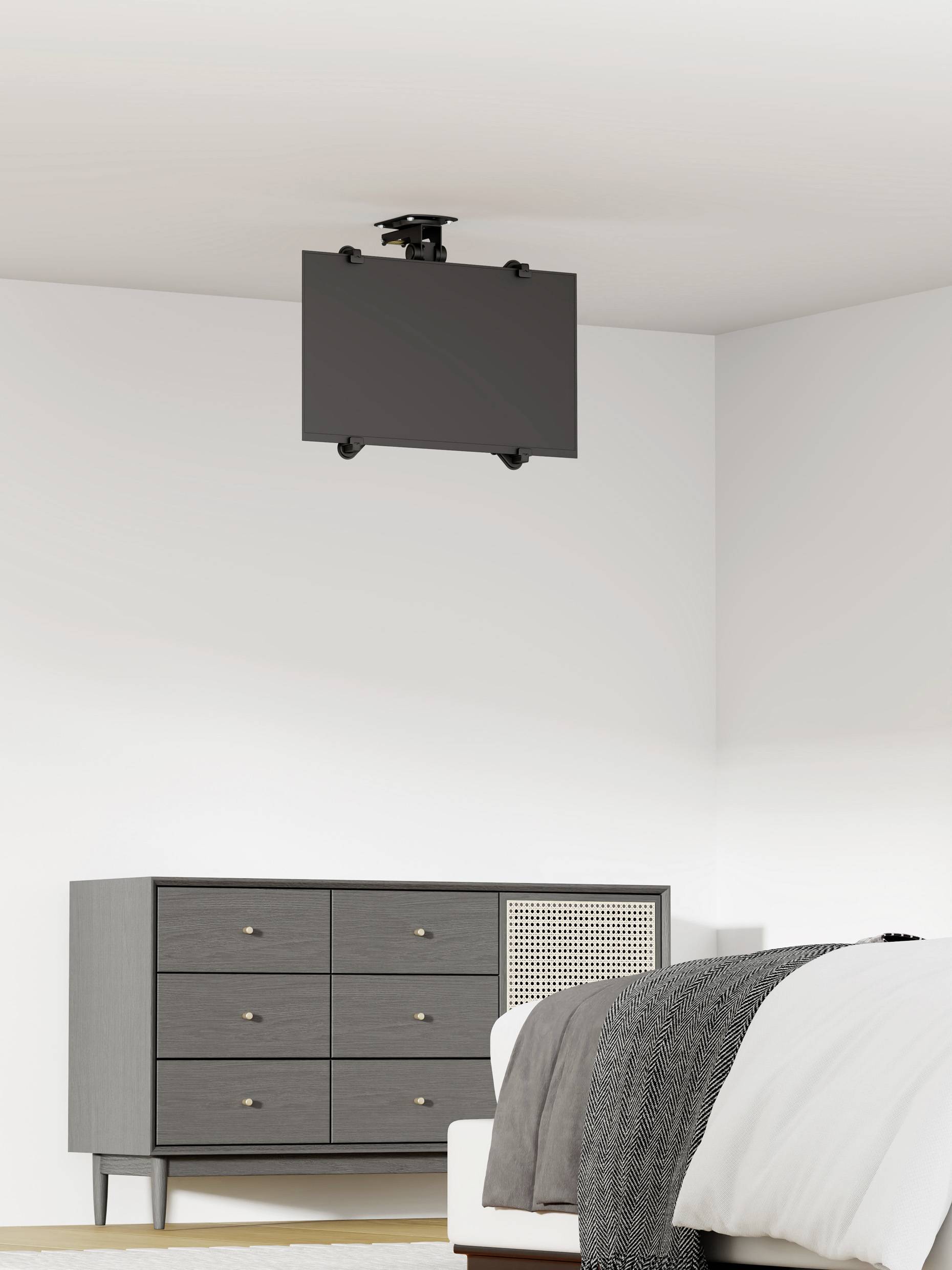 Ein grauer Raum zeigt eine Kommode links und ein Bett rechts. An der Decke hängt ein Flachbildschirm.