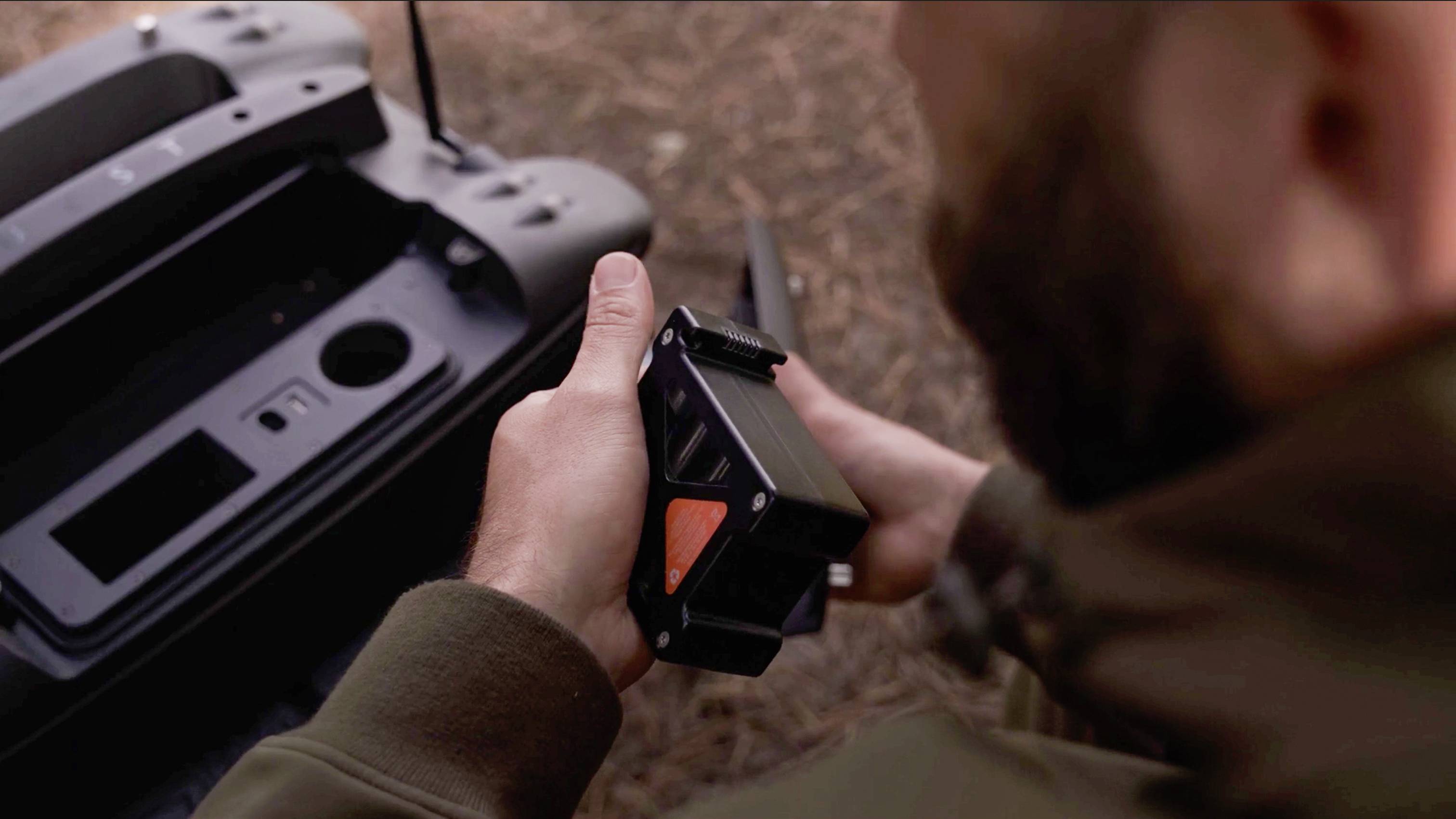 Person hält ein technisches Gerät mit einem markanten roten Element; daneben ein offenes Fach eines großen, dunklen Geräts.