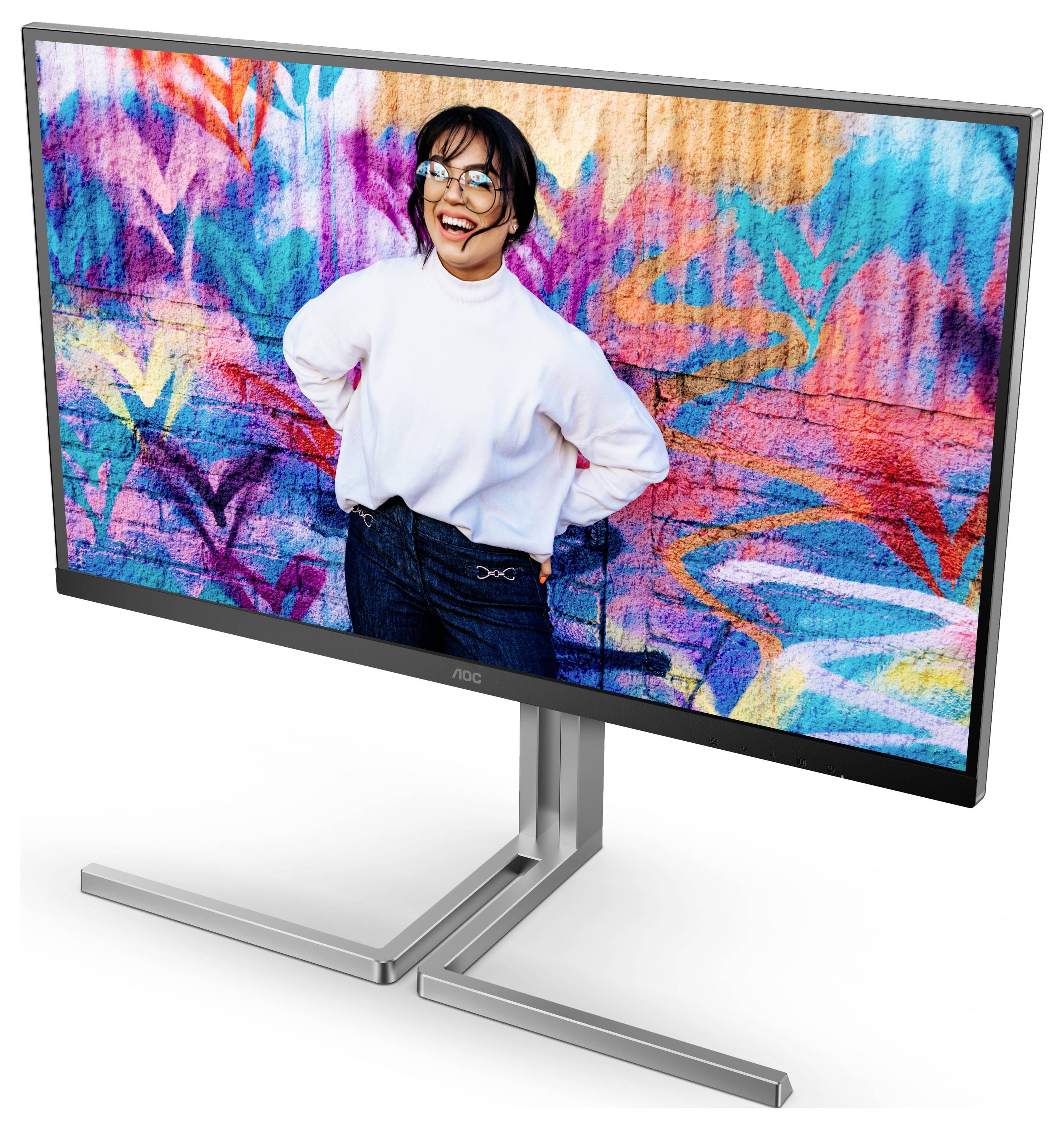 Eine lächelnde Person im weißen Pulli steht vor einer bunten, grafischen Wand. Sie hat die Hände in den Hüften und trägt eine Brille.