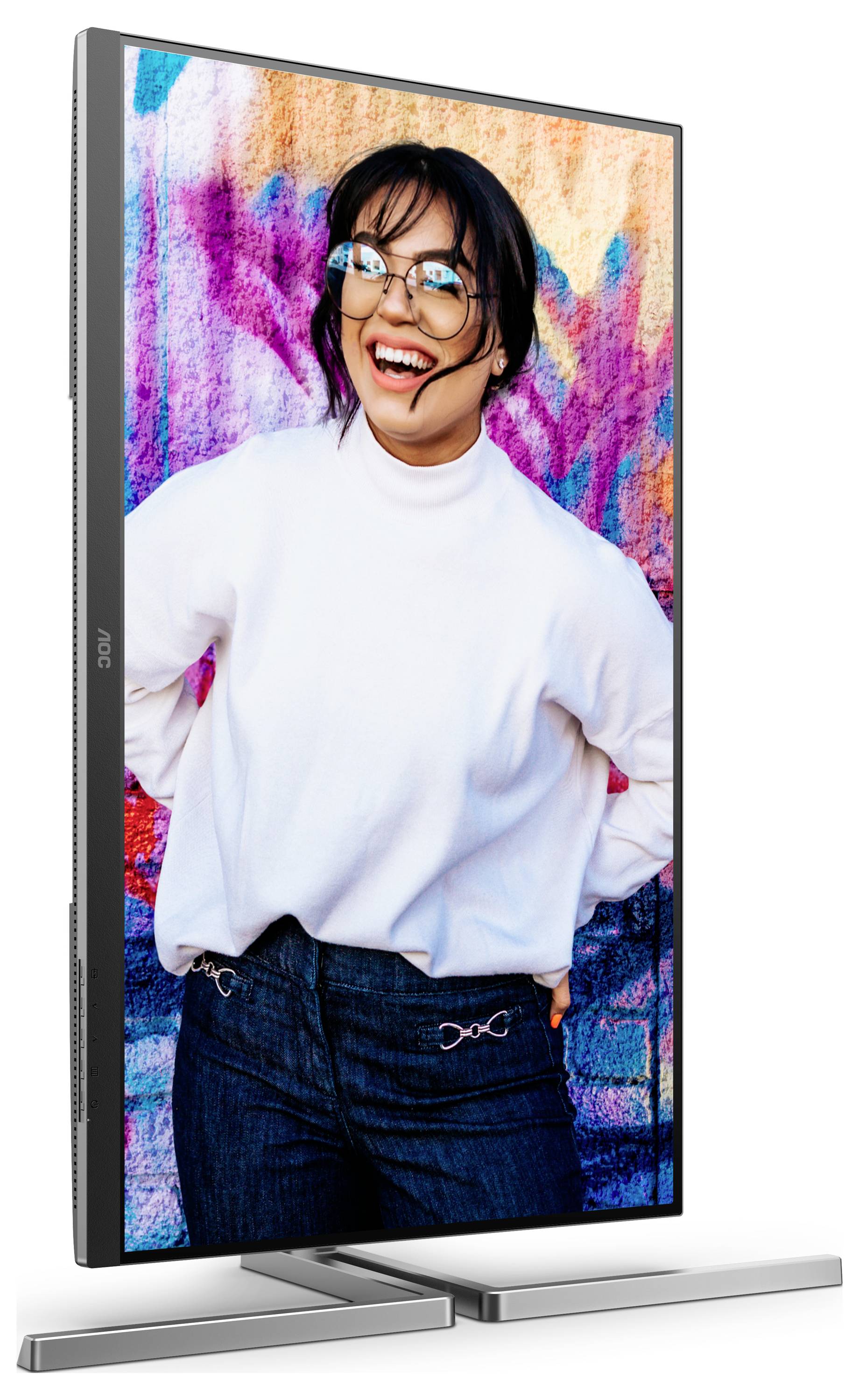 Eine lächelnde Person vor einer bunten, gesprühten Wand. Die Person trägt eine Brille, einen weißen Pullover und dunkle Jeans.