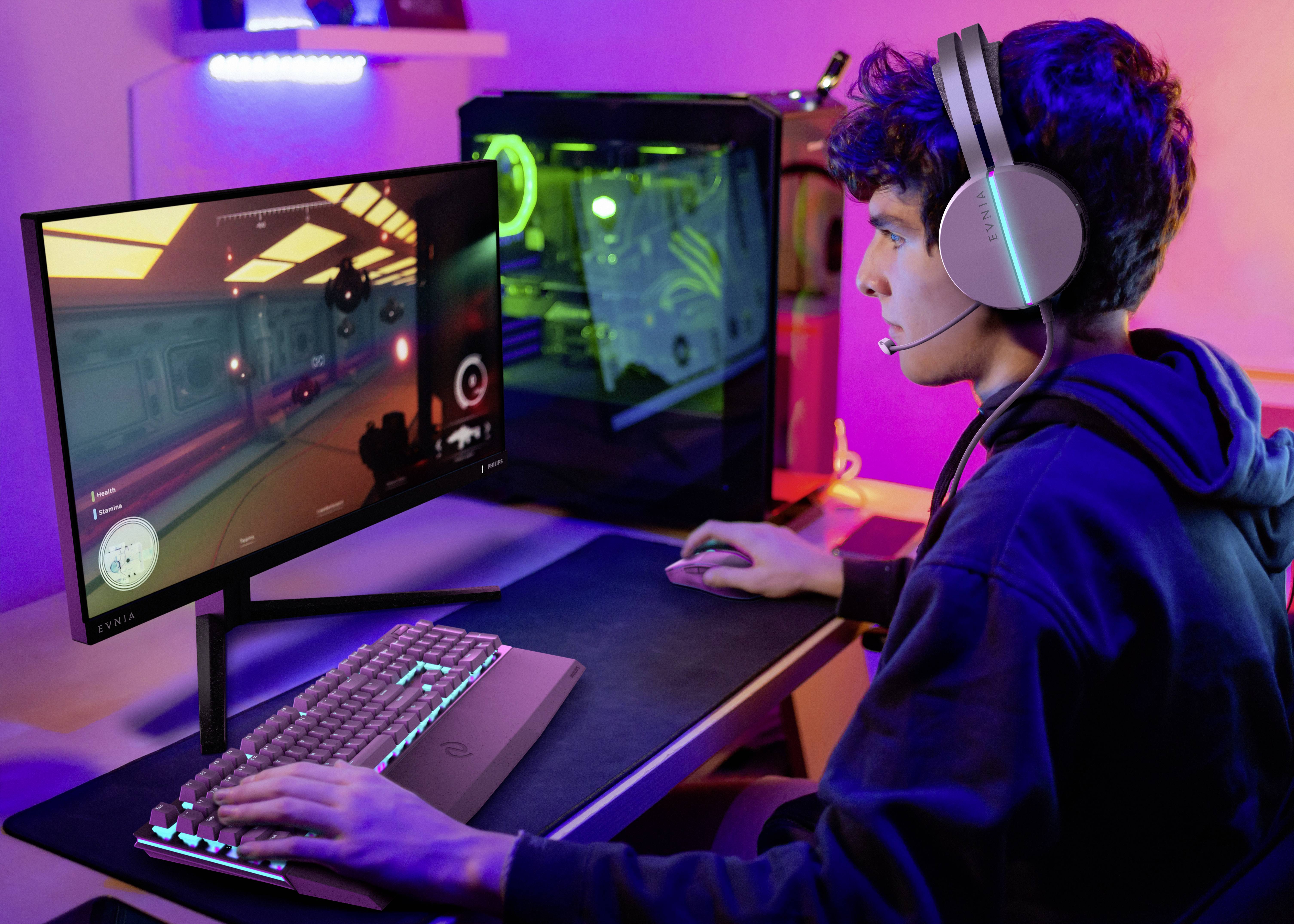 Ein junger Mann sitzt an einem Schreibtisch und spielt ein Videospiel auf einem Computer. Er trägt ein Headset und benutzt Tastatur und Maus.