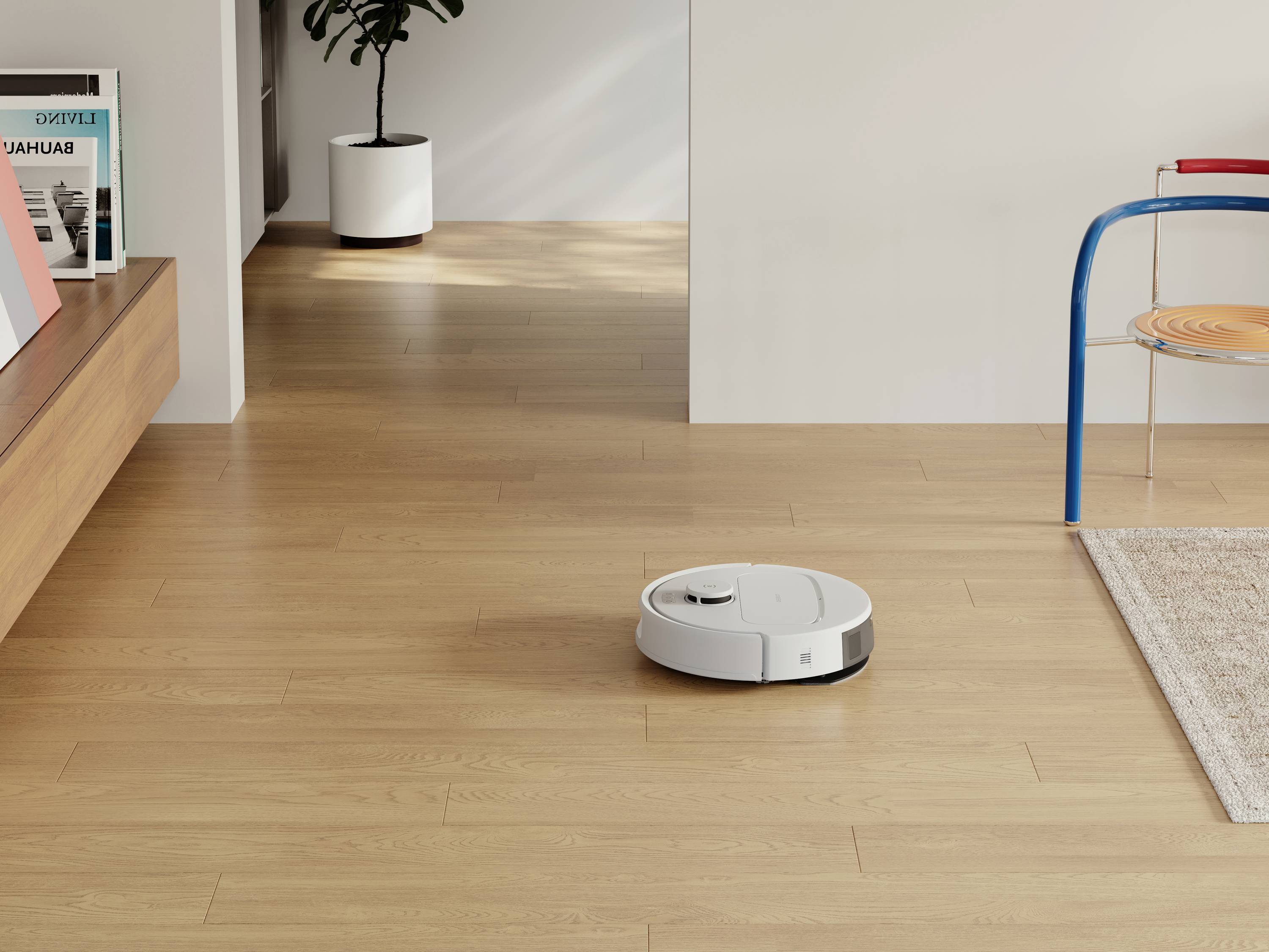 Ein weißer Saugroboter auf einem hellen Holzboden im Wohnzimmer, neben einem blauen Stuhl und einem Pflanzenkübel.