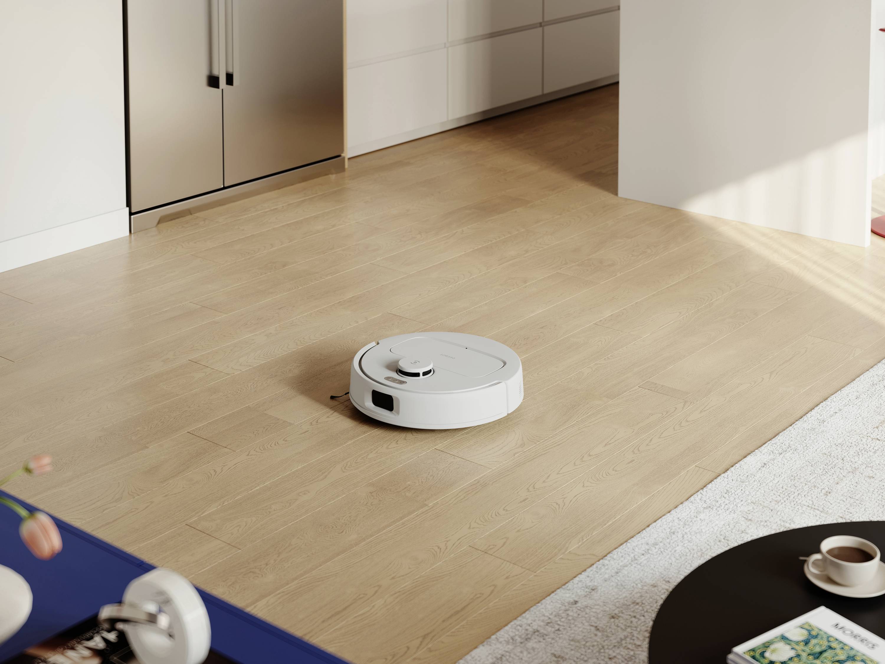 Ein Staubsaugerroboter reinigt den Holzboden in einem modernen Wohnzimmer. Im Hintergrund sind Küchenmöbel zu sehen.