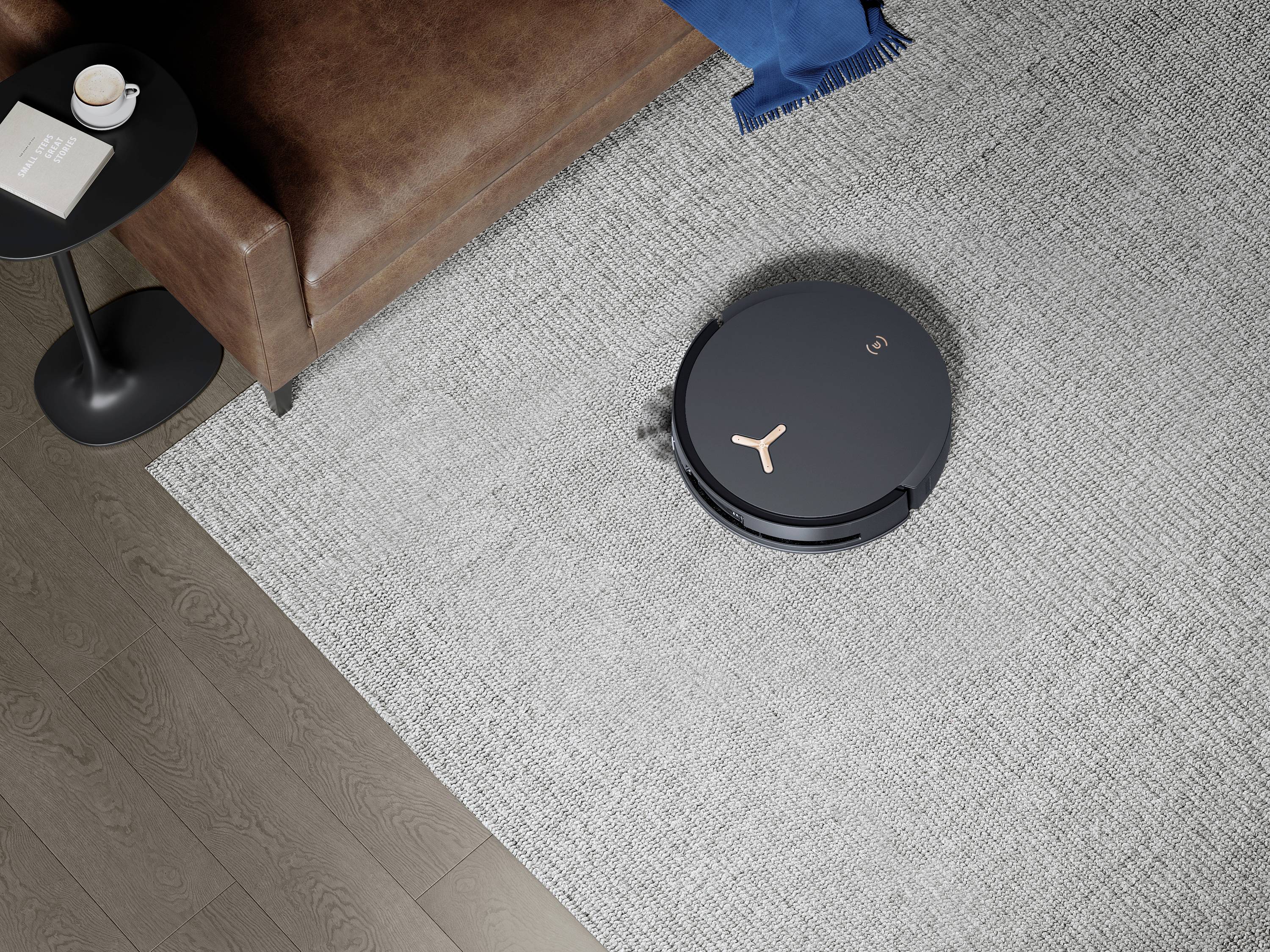 Ein runder Saugroboter reinigt einen grauen Teppich neben einem braunen Ledersofa. Ein Beistelltisch mit einem Buch und einer Tasse steht neben dem Sofa.