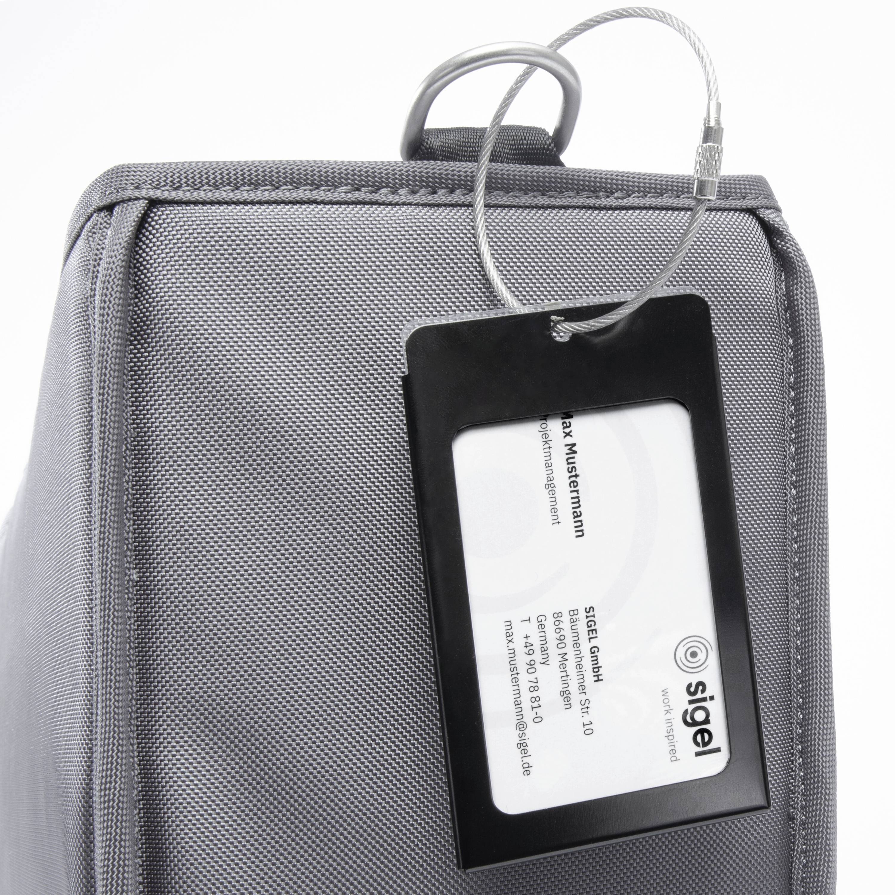 Graue Tasche mit Namensschild an einer Seite, darauf steht 'Max Mustermann', darunter die Adresse von 